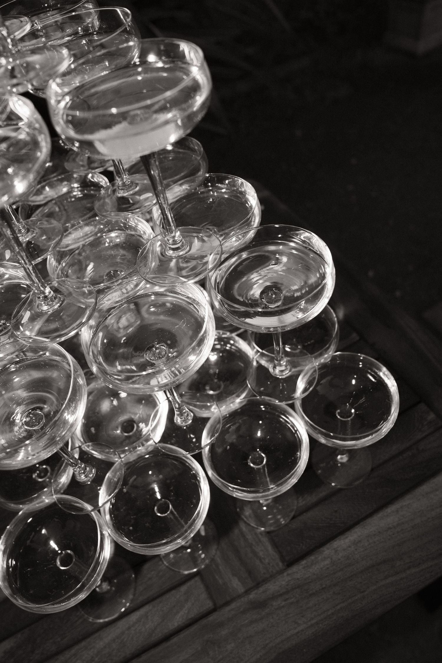 Elegant champagne coupe glasses arranged in rows on a dark surface at a wedding reception.