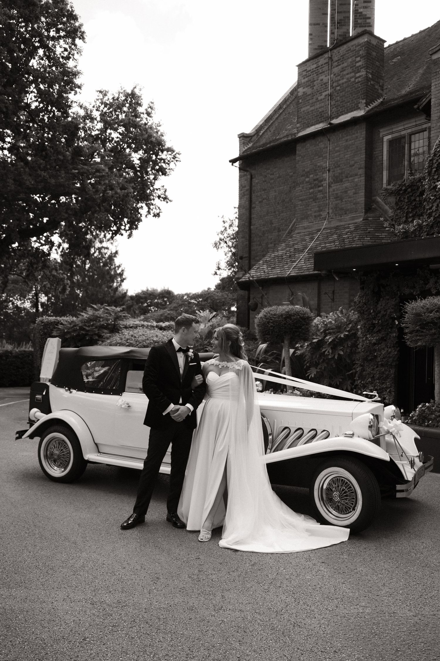 Classic vintage car decorated for a wedding with white ribbons parked outside a brick building.