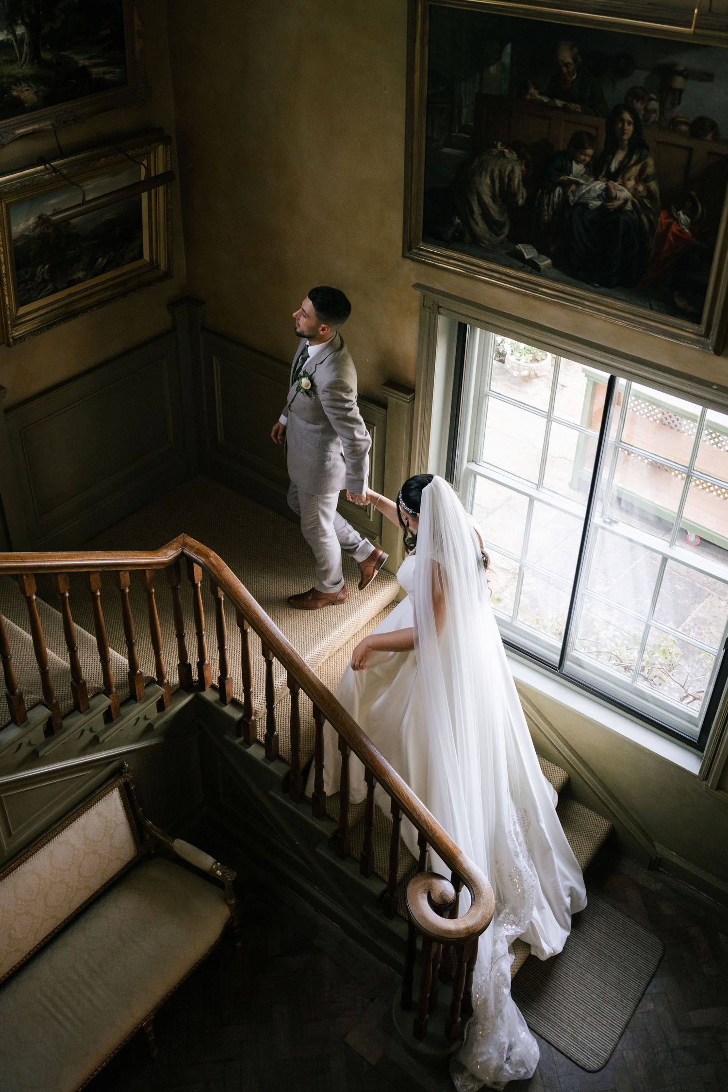 Wedding dress flowing down historic staircase with natural window light.
