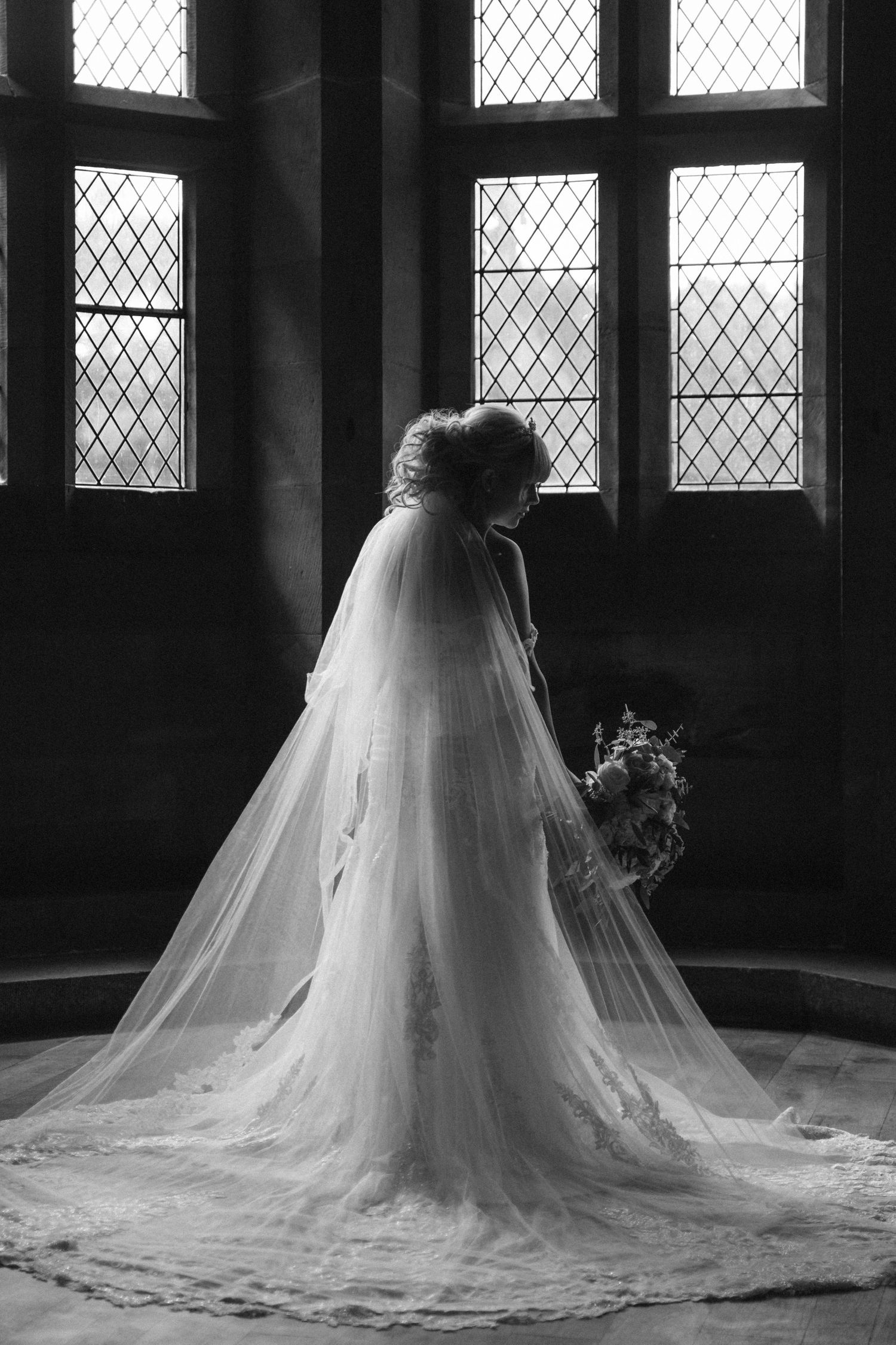 Elegant wedding dress silhouette against gothic windows in dramatic black and white.