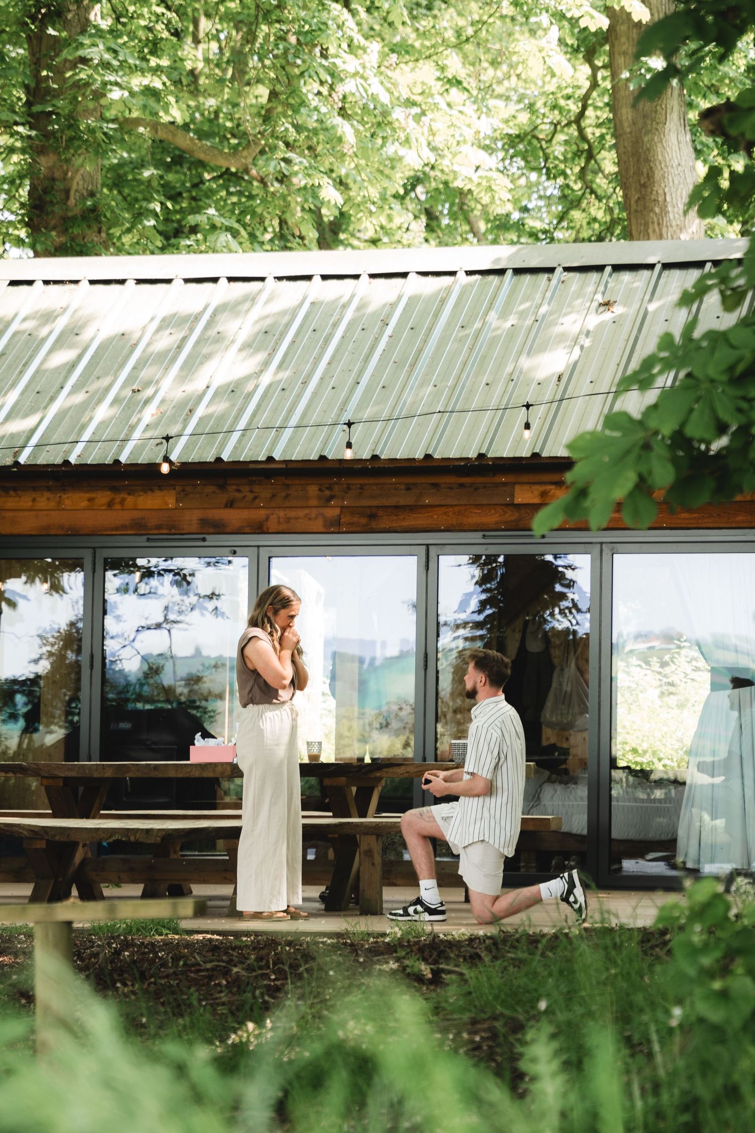 A romantic scene unfolds on a rustic wooden deck surrounded by lush green foliage.