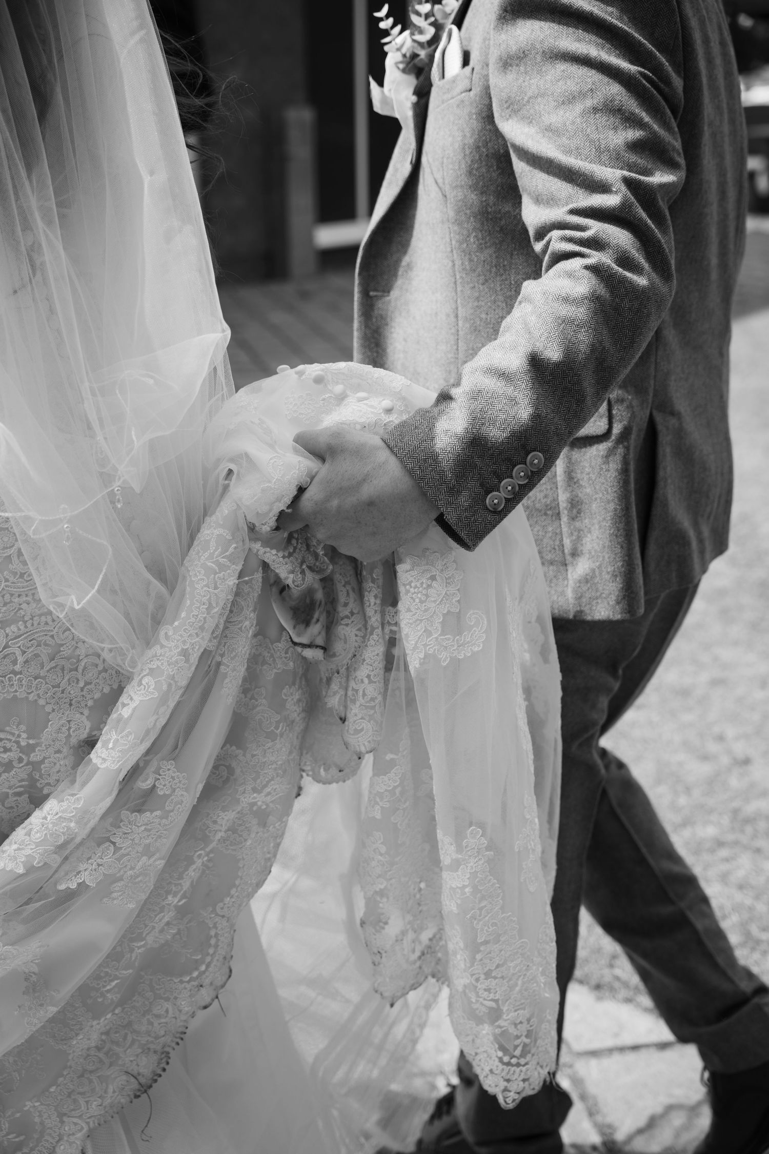 Close-up black and white photos showing details of a bride's white lace wedding dress and groom's formal attire.