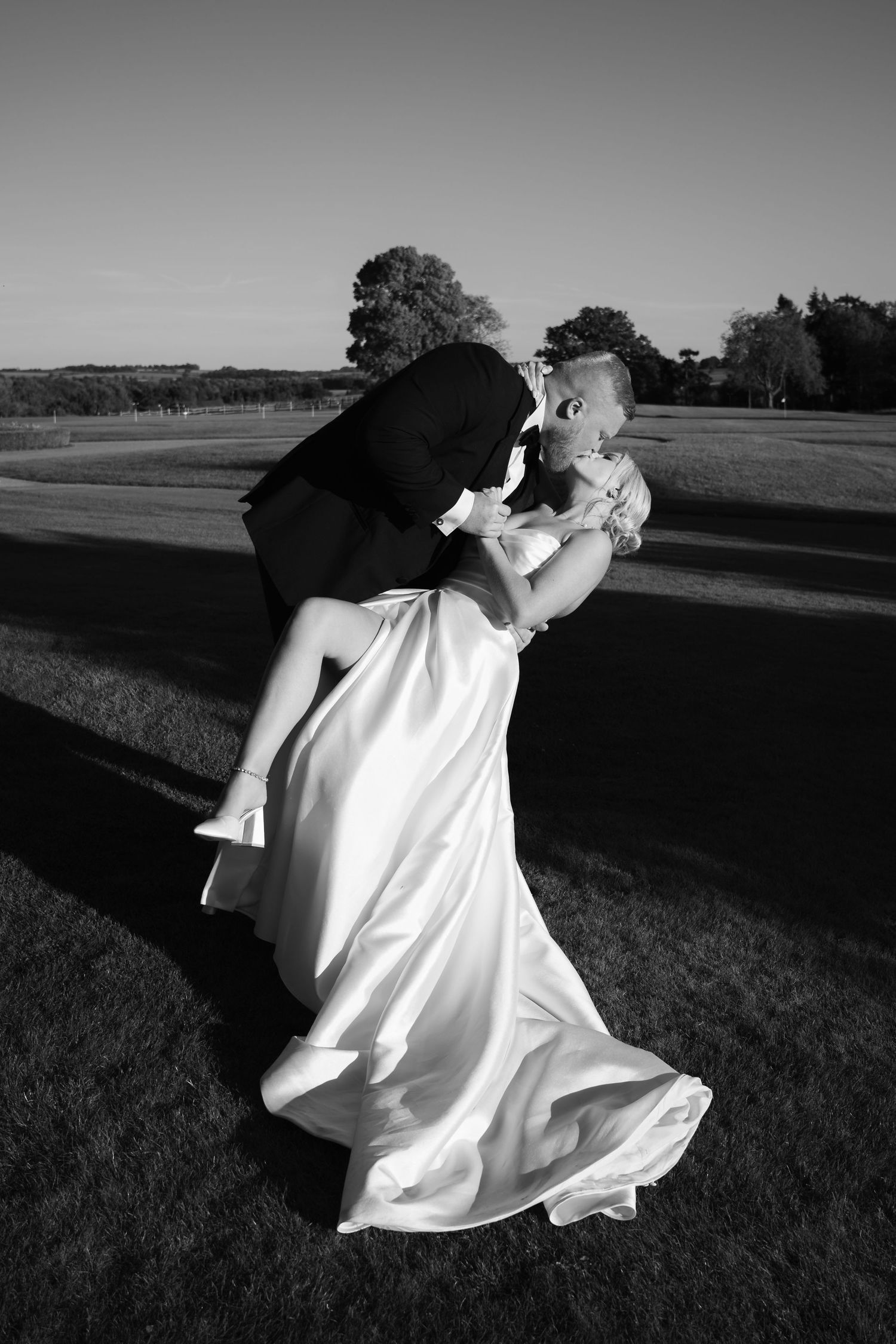 A series of black and white photographs showing a figure in white clothing dancing gracefully across a grassy field at sunset.