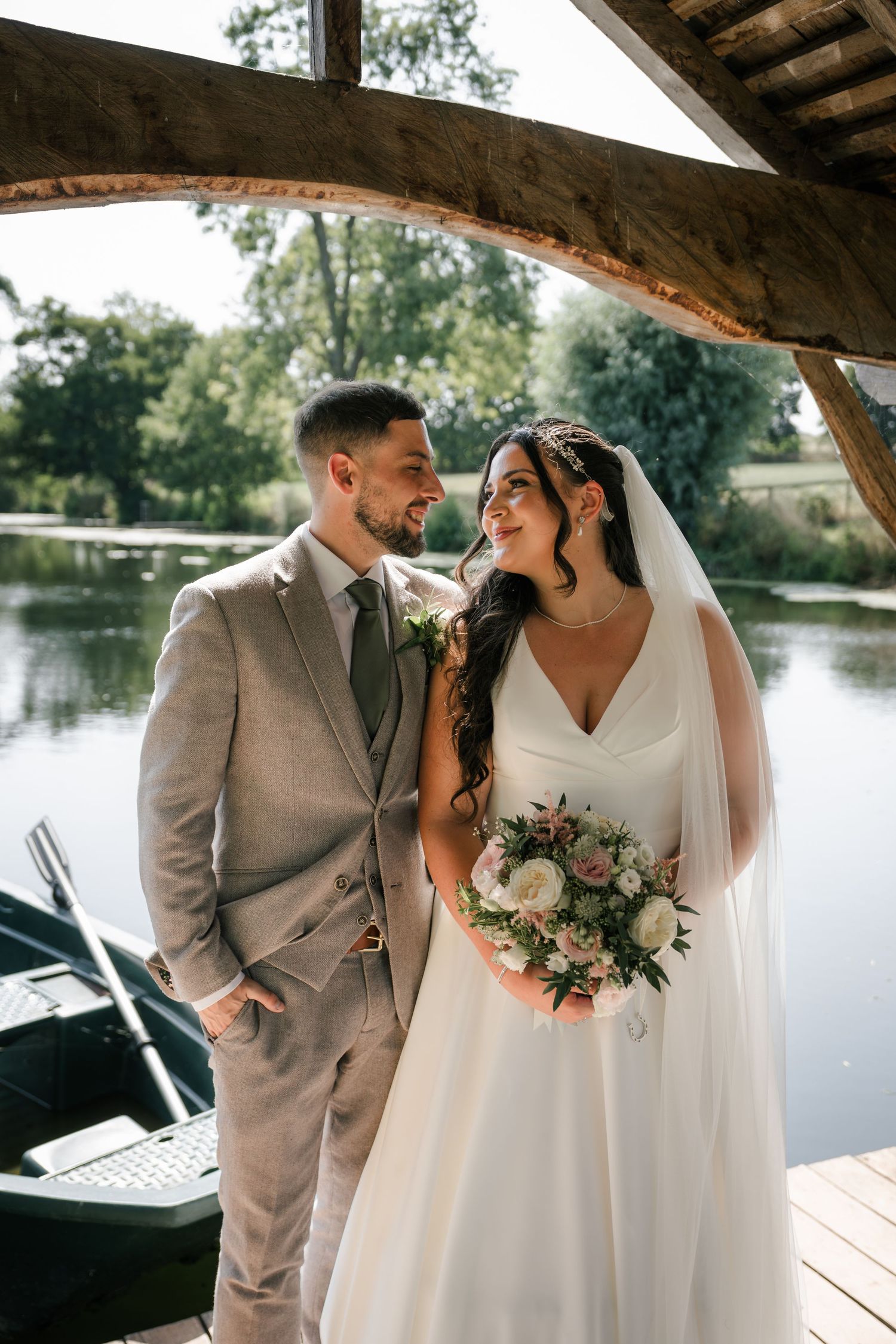 A romantic wedding couple shares tender moments under a wooden gazebo by a serene lake.