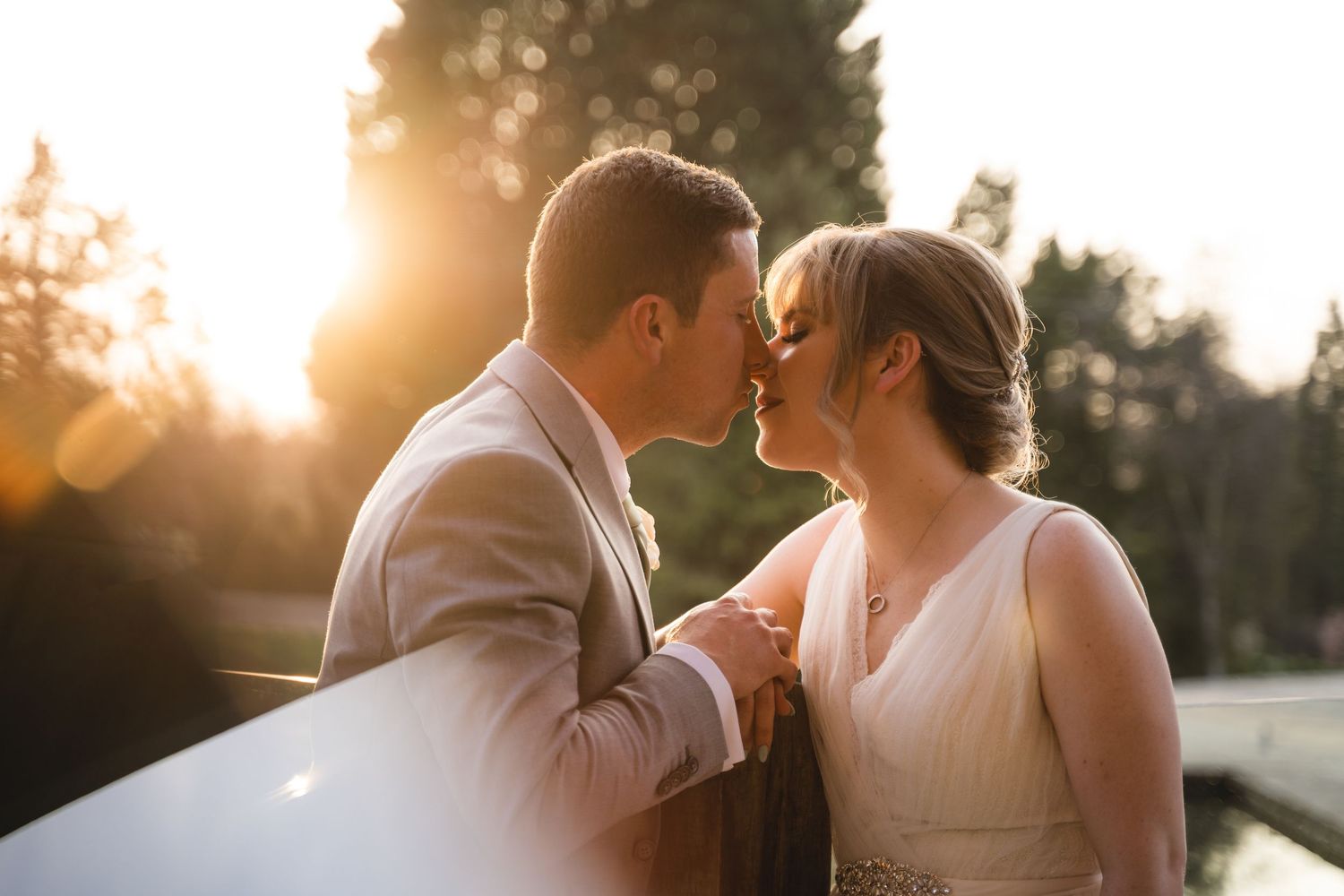 A bride and groom share an intimate moment at sunset with golden light streaming through the trees behind them.