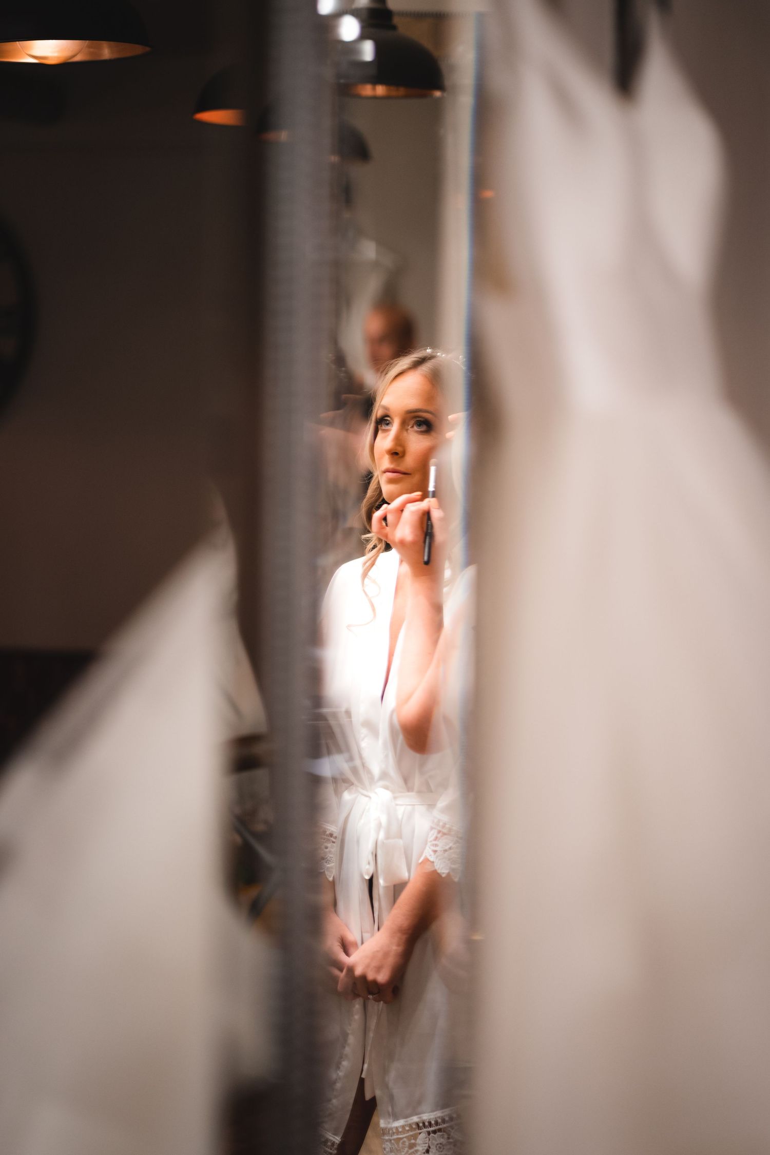A dreamy portrait through a doorway showing a figure in soft light wearing a white outfit with pendant lighting above.
