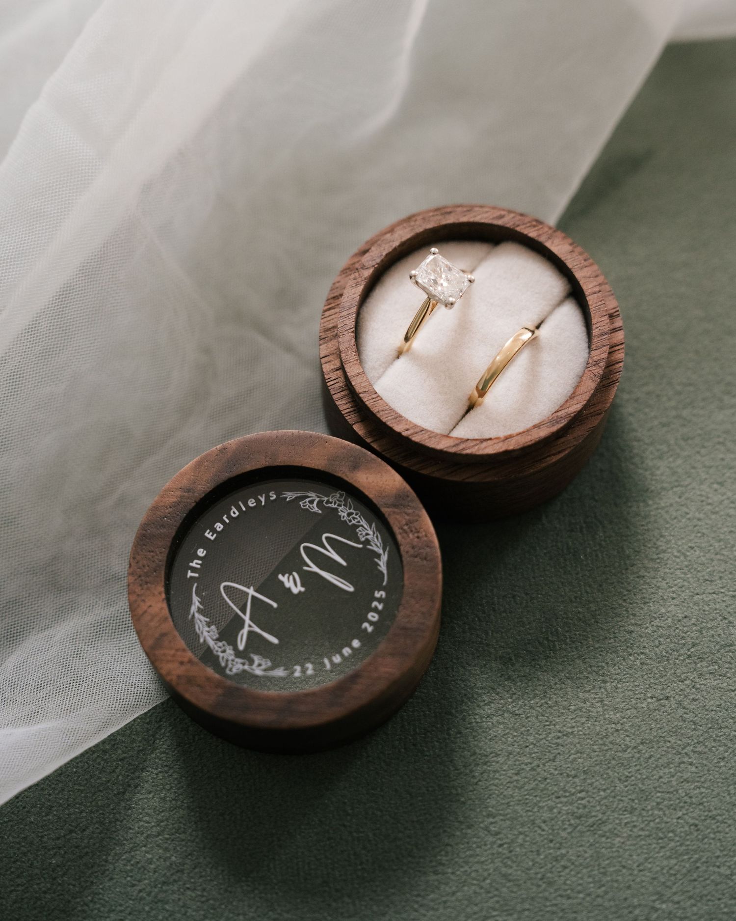 Wooden ring boxes with custom engravings displayed on green surface.