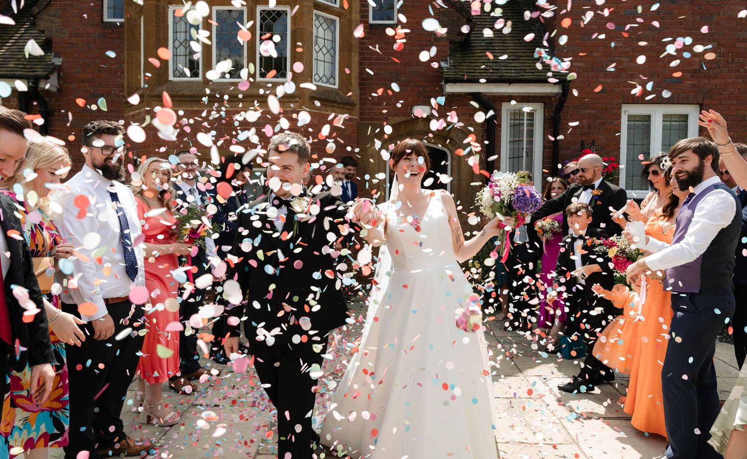Wedding guests shower the newlyweds with white confetti petals during an indoor celebration at a brick venue.