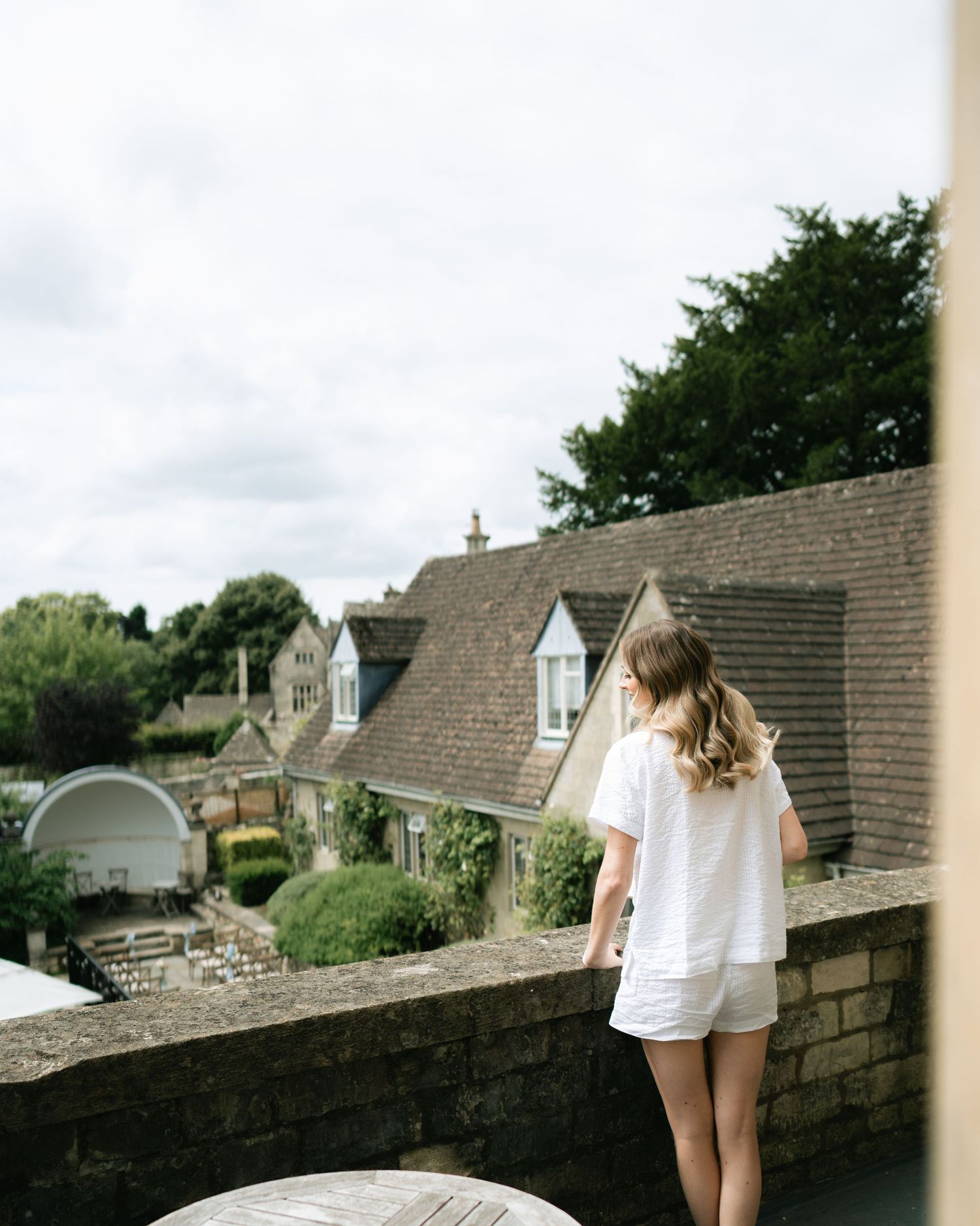 A person in a white shirt sits on a stone wall overlooking a scenic residential area on a cloudy day.