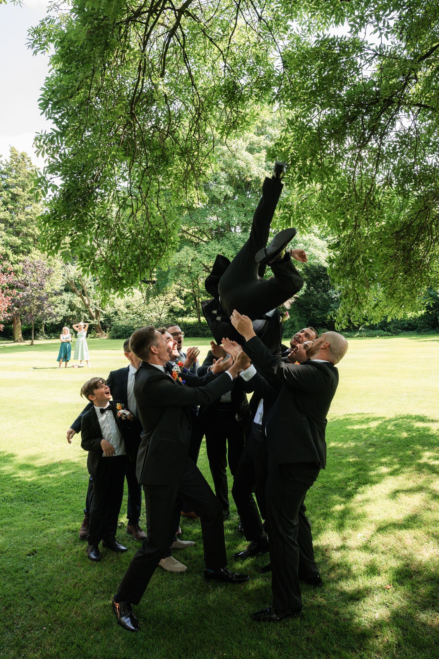 Wedding party having fun and posing playfully on a sunny lawn with trees.
