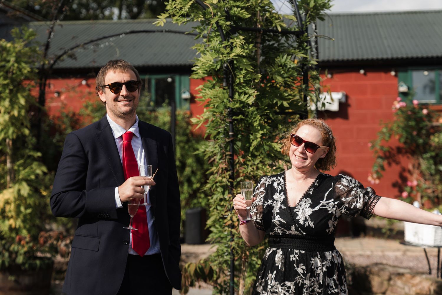 People in formal attire enjoying drinks and conversation at an outdoor garden party on a sunny day.