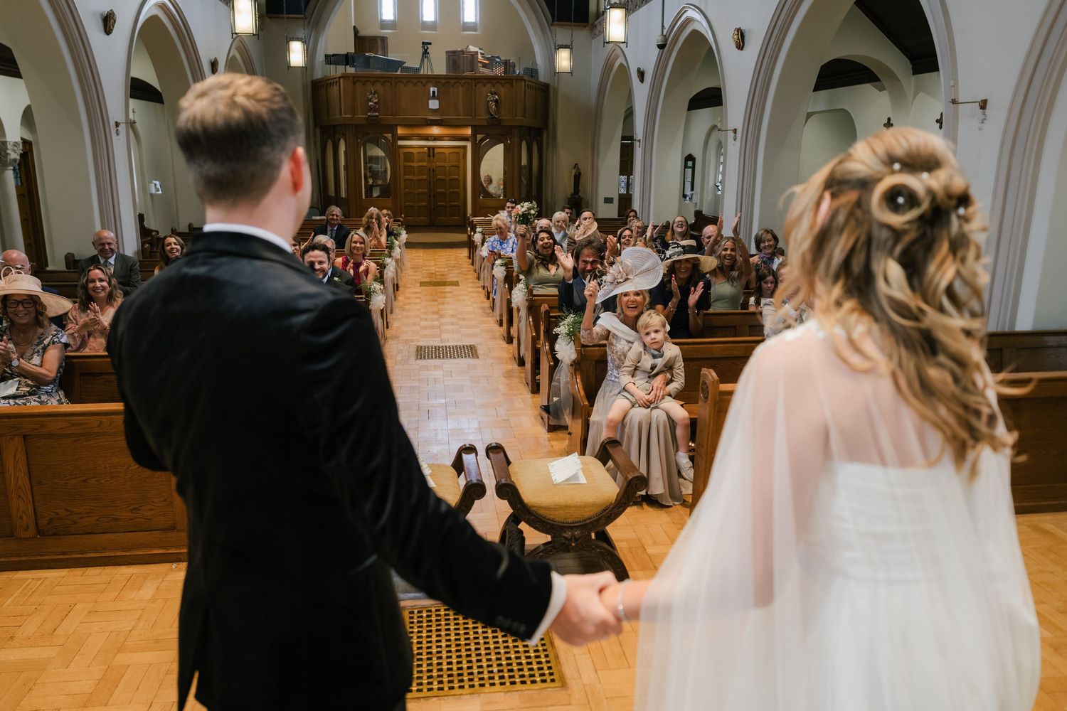 A couple holding hands during their wedding ceremony in a traditional church with arched ceilings and wooden pews.