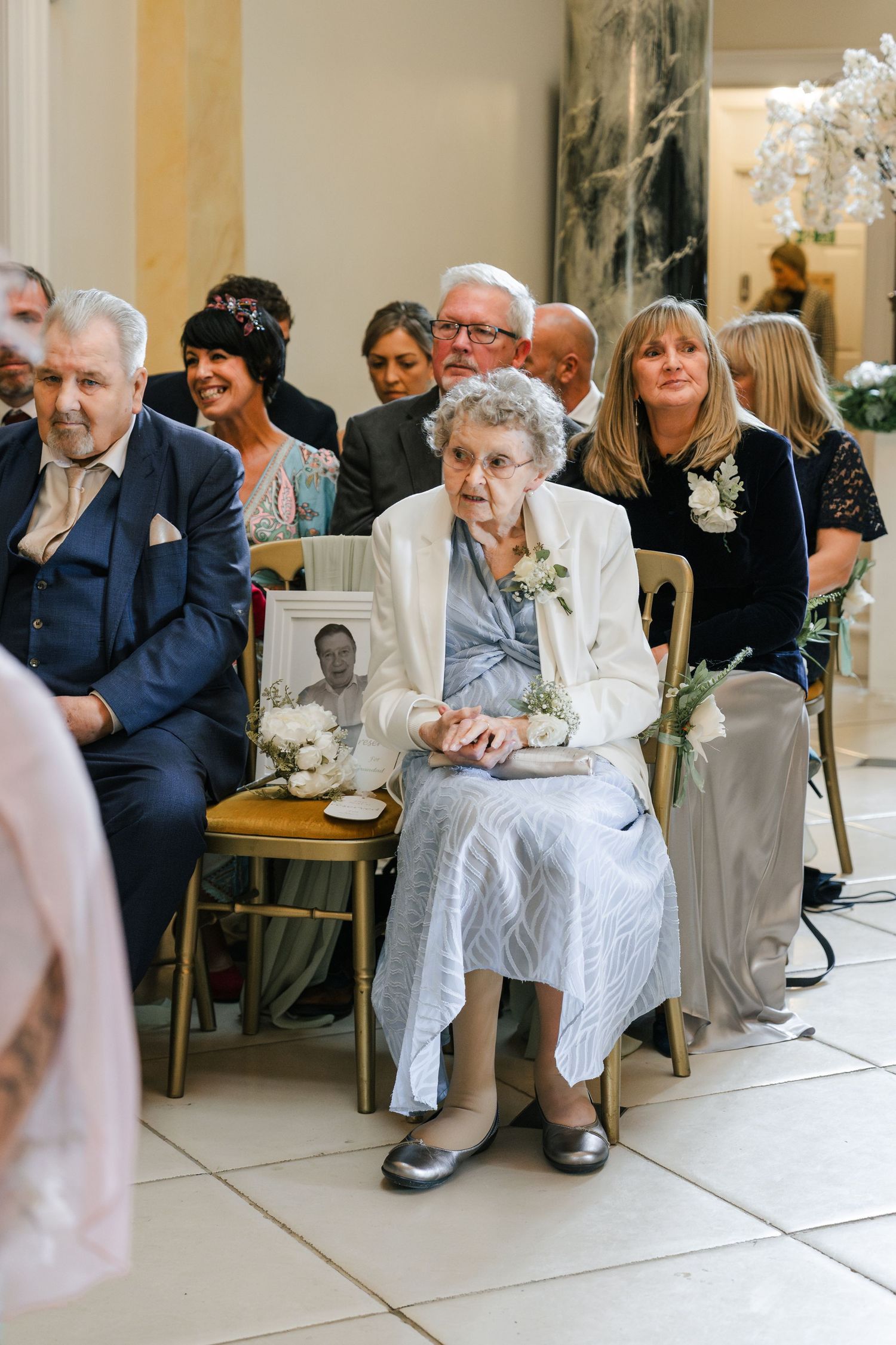 People seated in chairs along a wall at what appears to be a formal gathering or waiting room.