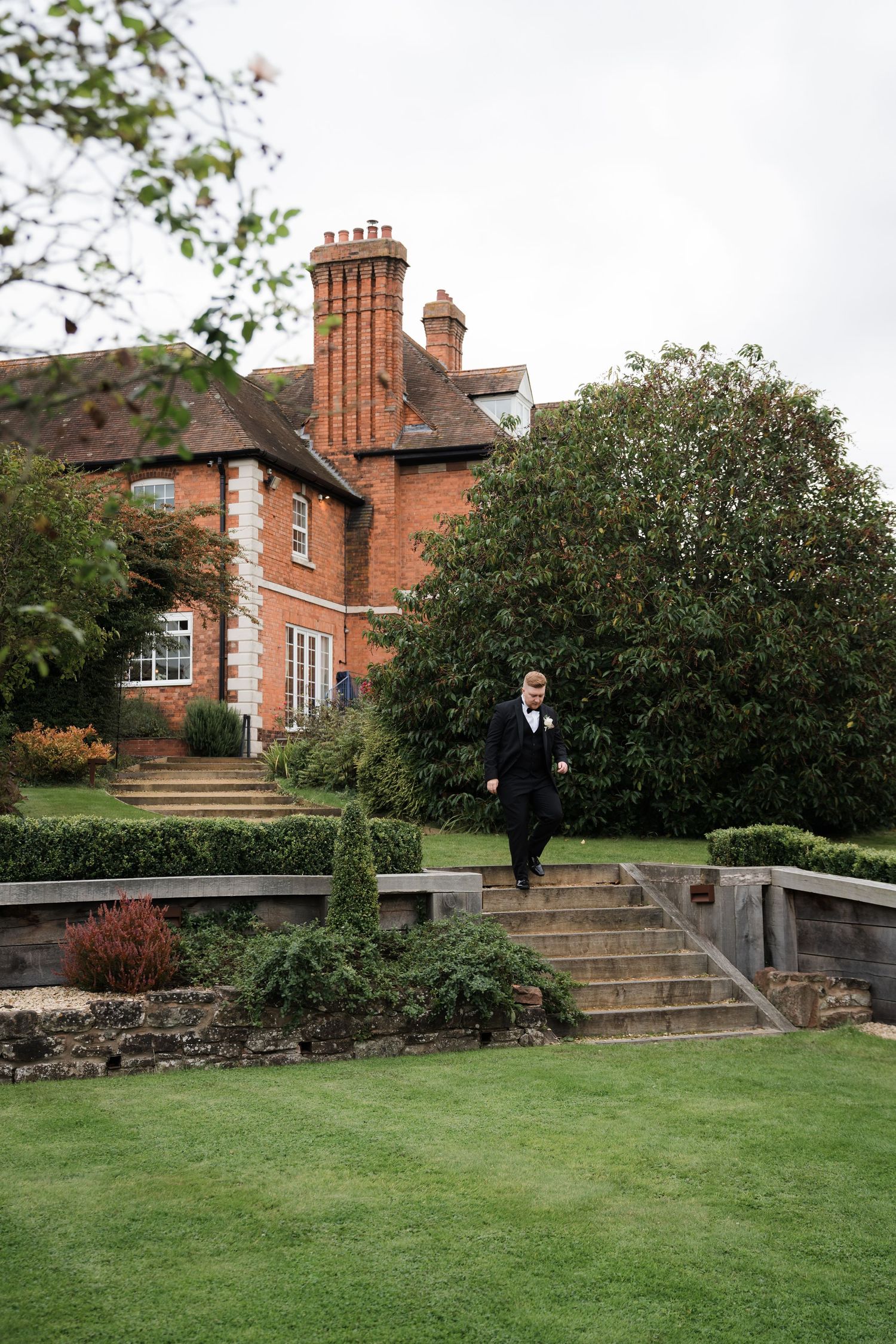 Stone steps lead up to a historic red brick mansion with manicured lawns and gardens.