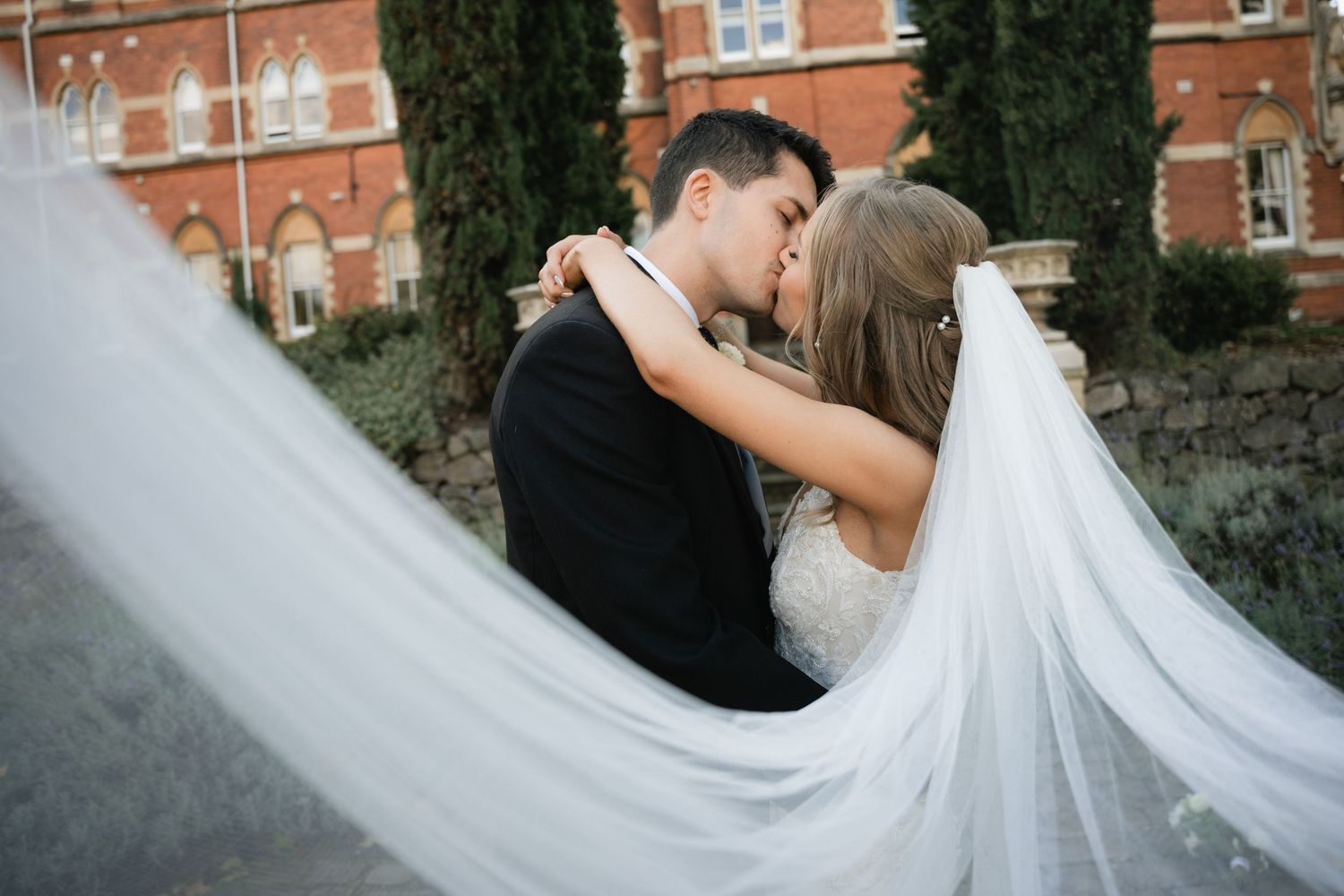 A flowing white wedding veil billows in the breeze as a couple shares an intimate moment together.