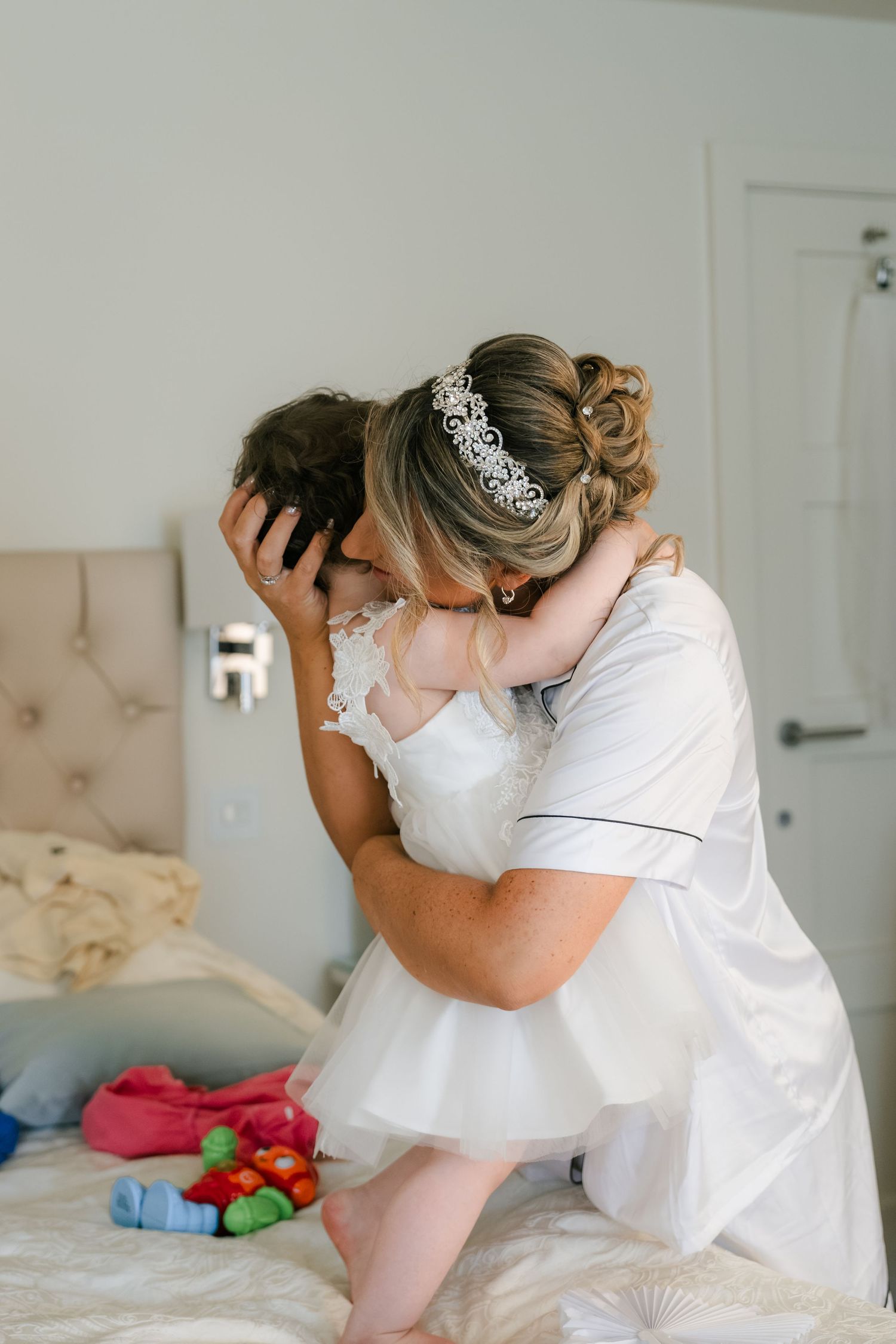 A tender moment captured in white as someone holds and comforts a small baby on a bed.