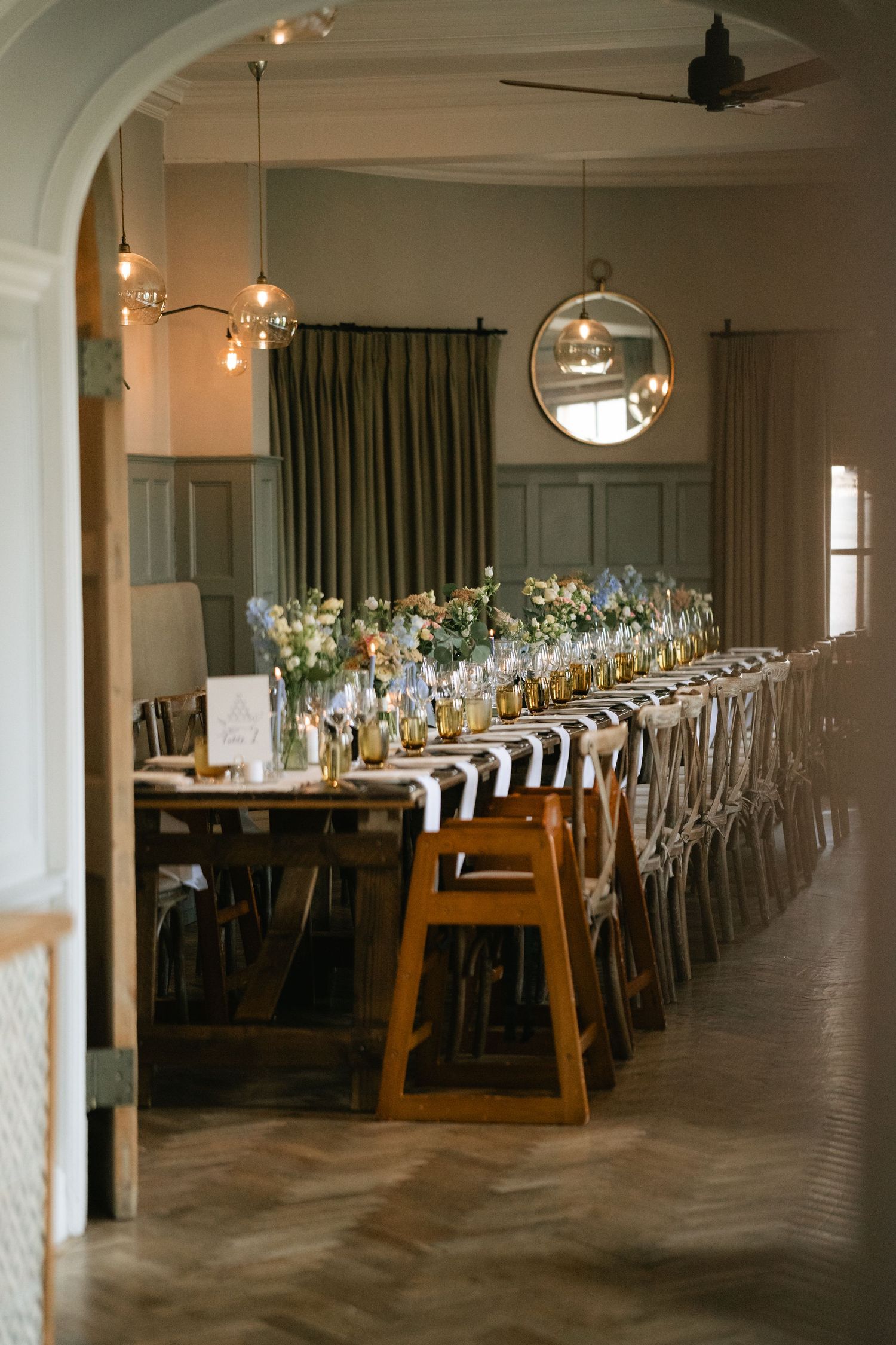 An elegant wedding reception venue with long wooden tables set for dinner under modern globe pendant lights.