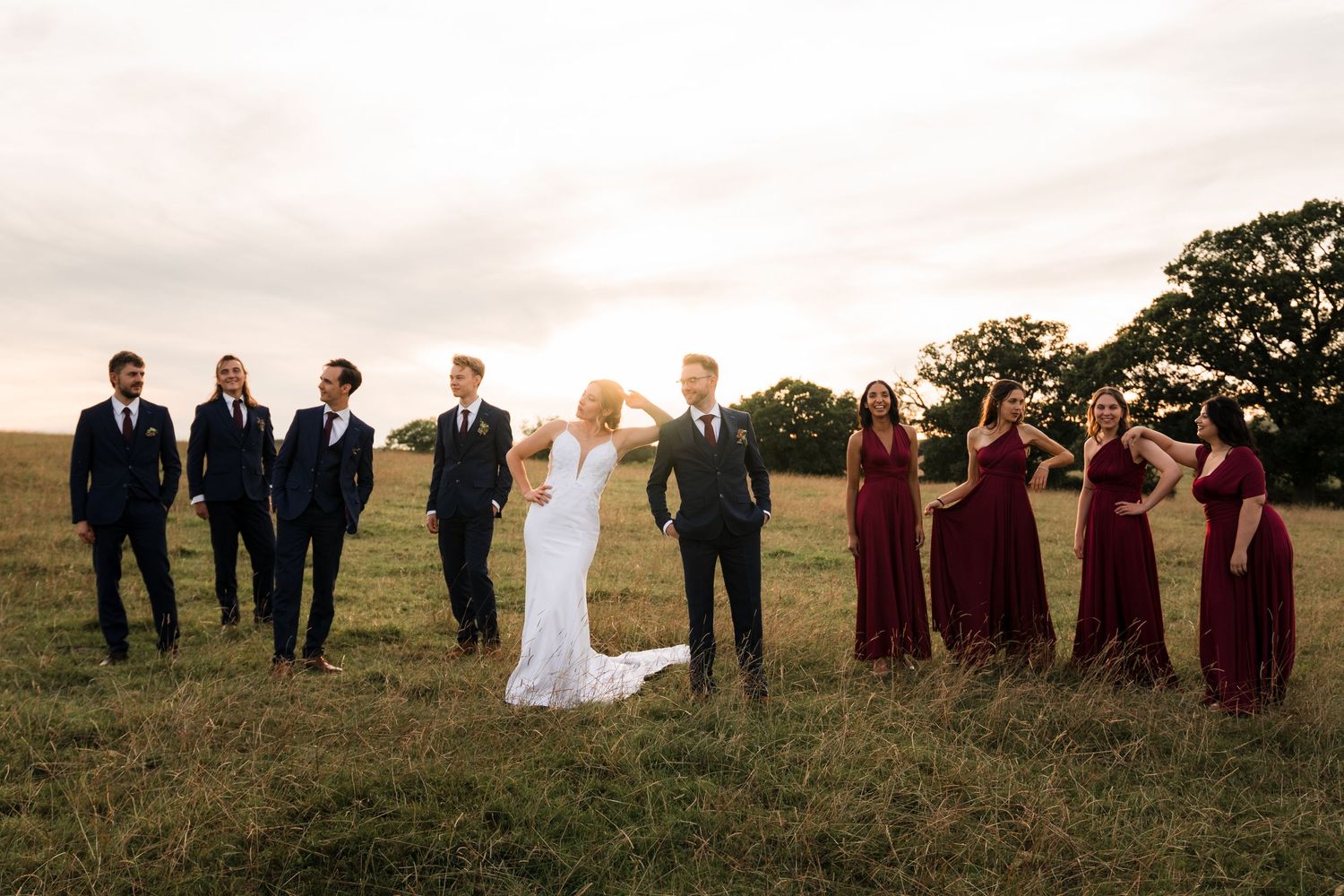 Wedding party poses in a line against a sunset backdrop.