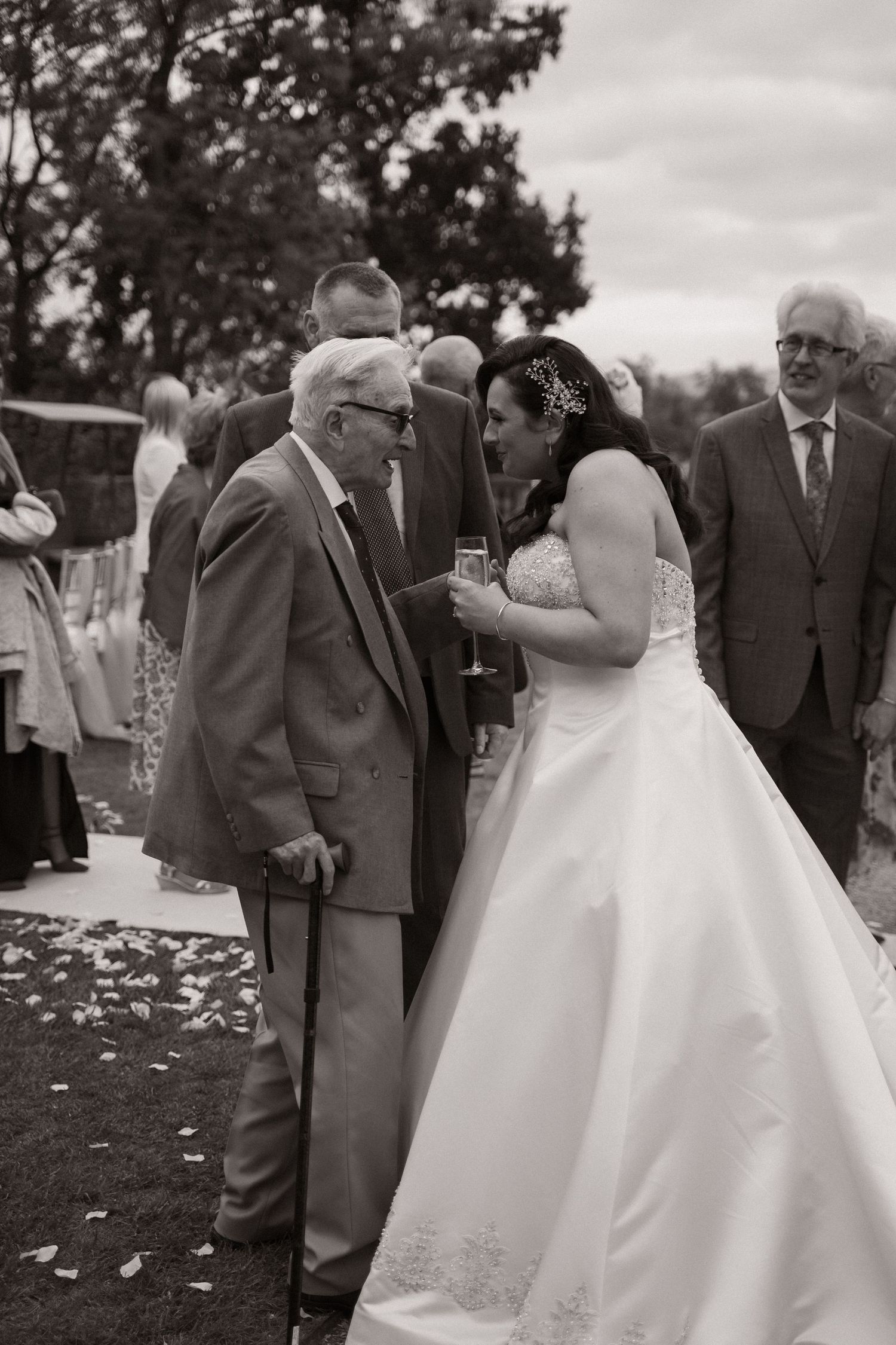 Black and white photo sequence shows emotional moments between a bride in white dress and elderly man at outdoor wedding.