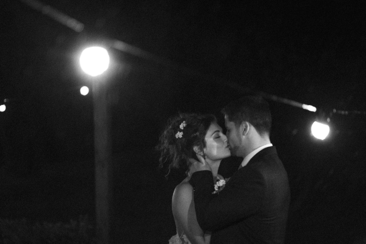A romantic black and white nighttime dance captured under glowing outdoor lights.