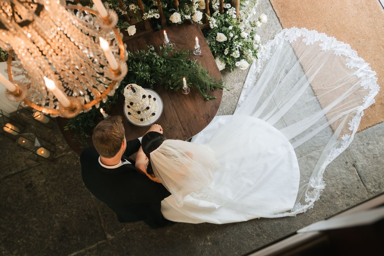 Aerial view of bride and groom kneeling at altar with lace veil spread on floor during wedding ceremony.