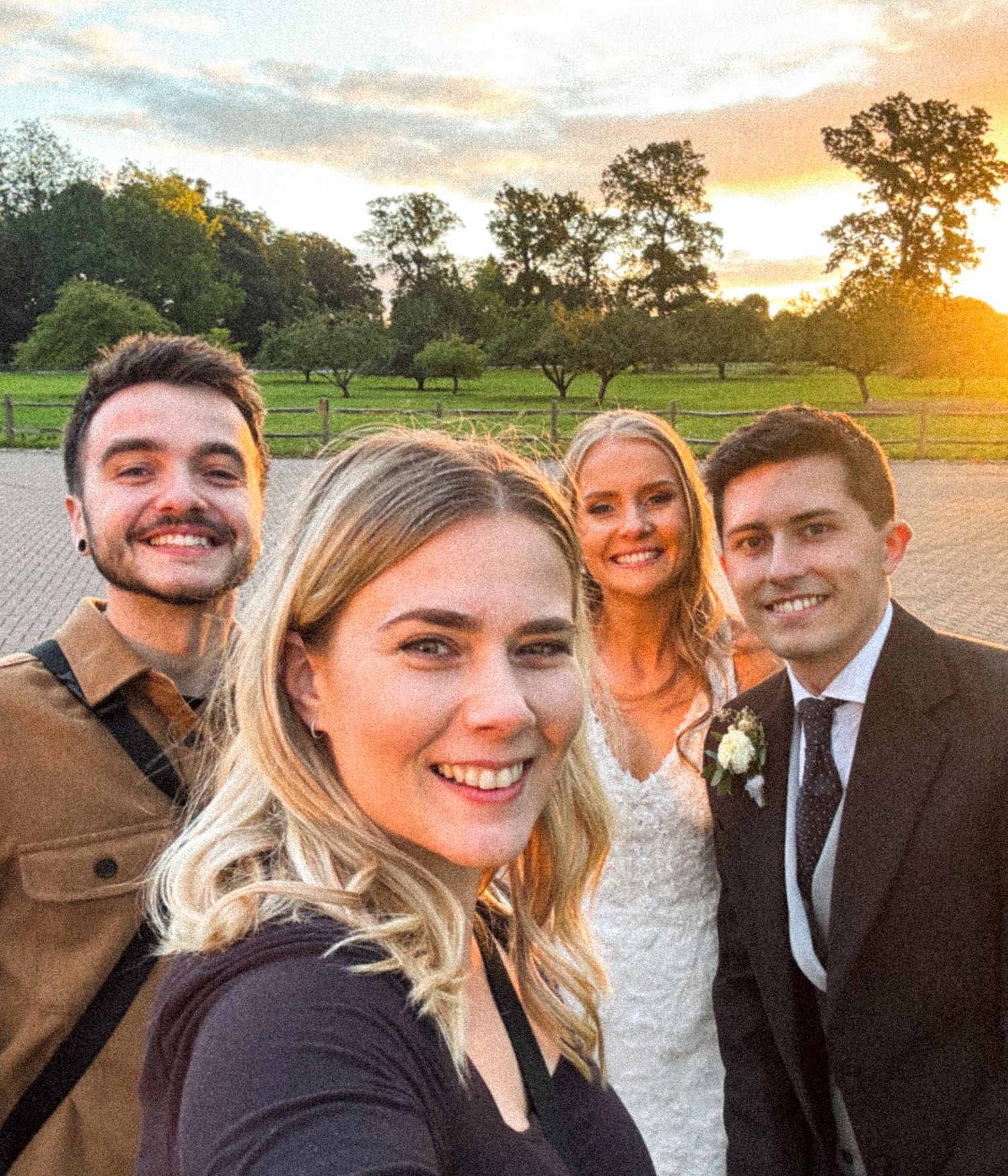 A group of wedding guests pose together for sunset photos in an outdoor setting with golden sunlight.