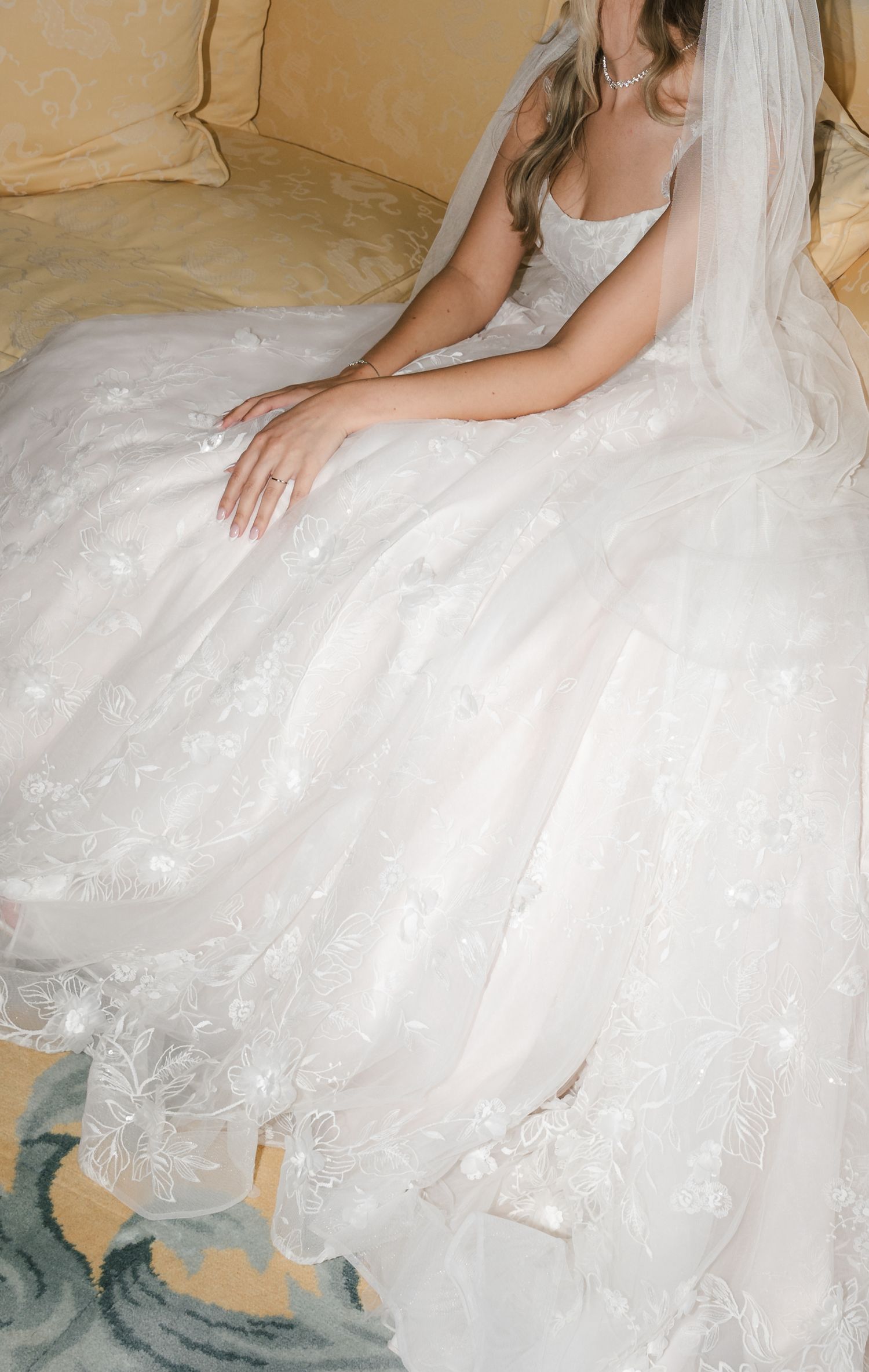 Close-up view of a white tulle wedding dress with delicate lace details spread out on a beige floor.