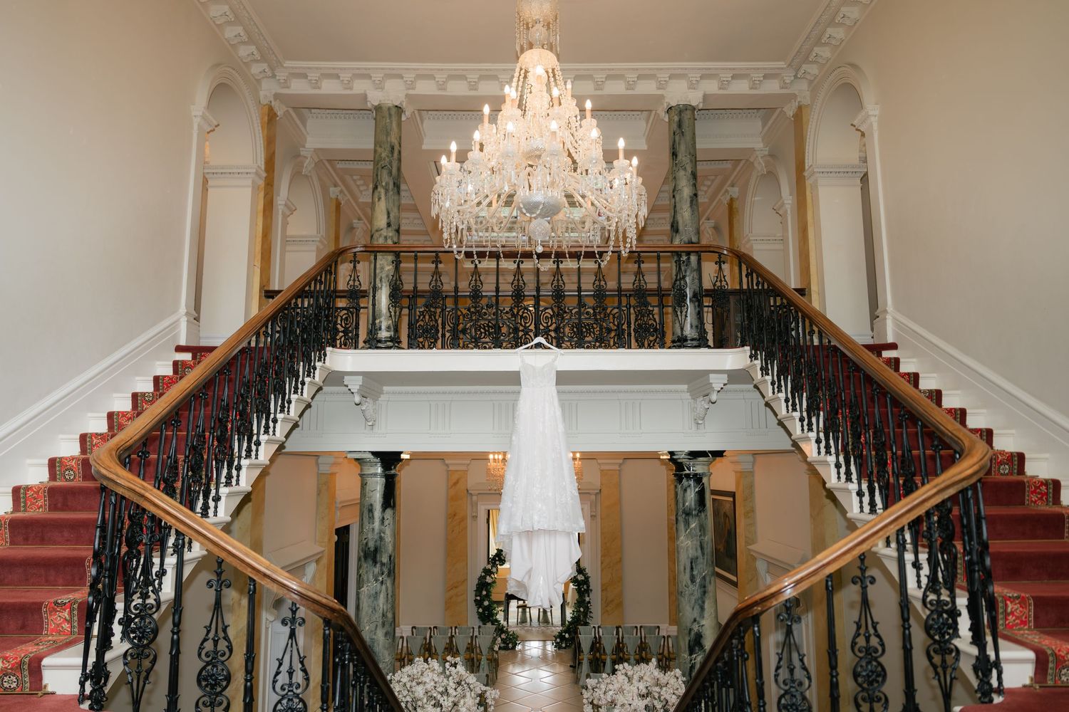 Elegant grand staircase with red carpet and crystal chandelier in luxurious mansion interior.
