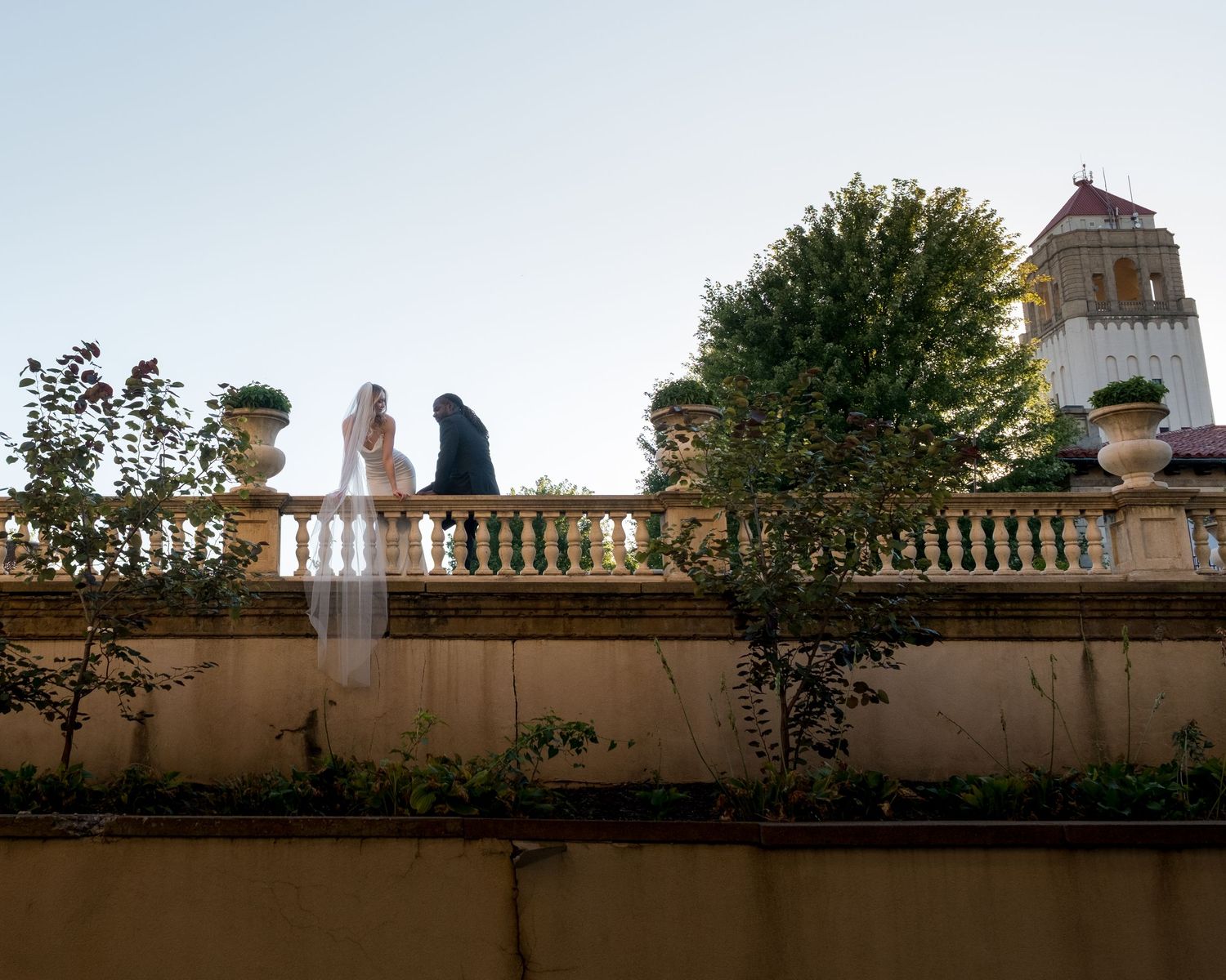 Newlywed couple embrace on a stone terrace during an intimate wedding, historic architecture in the background.