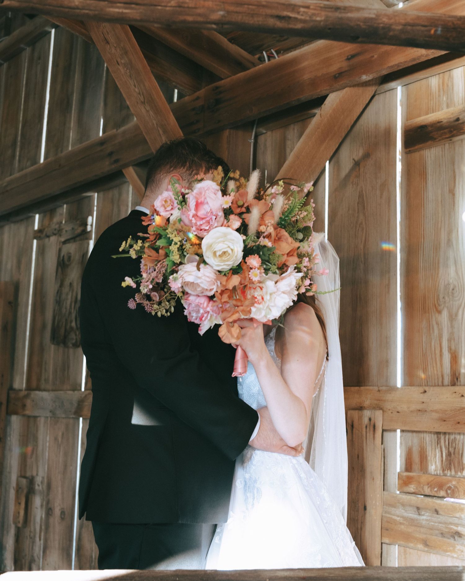 A rustic barn wedding scene with elegant floral arrangements and natural light streaming through wooden slats.