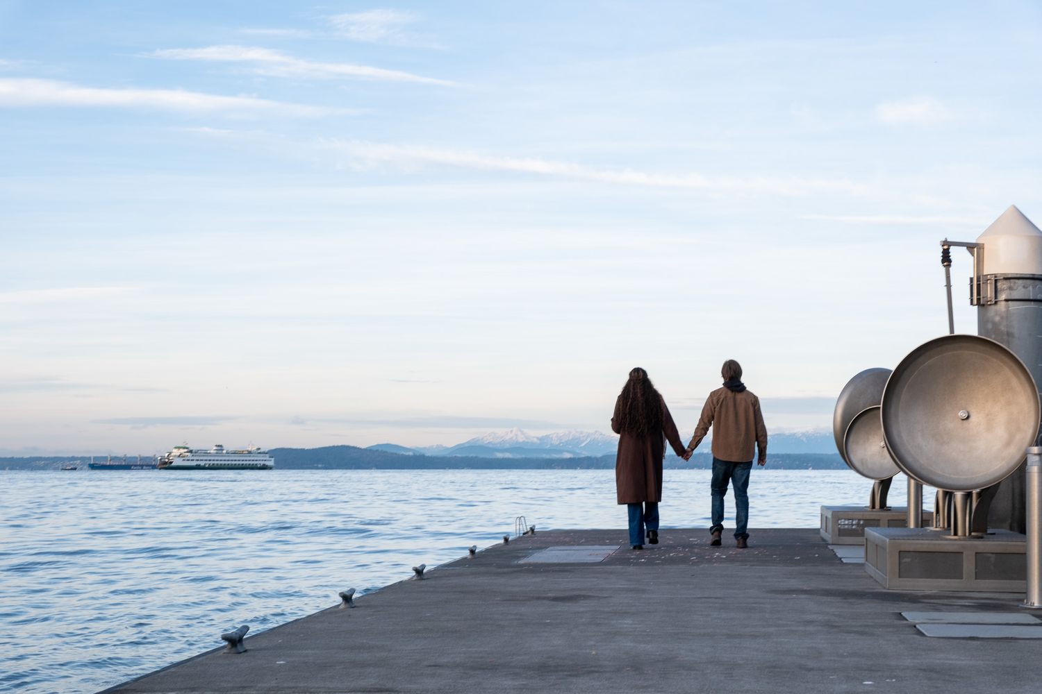 A scenic pier extends into the ocean at sunset with silhouetted figures walking along its length.