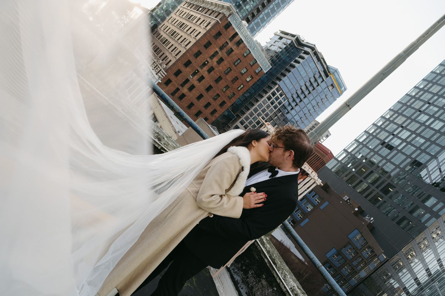 A couple shares an intimate moment during their wedding photoshoot against a backdrop of modern city buildings.