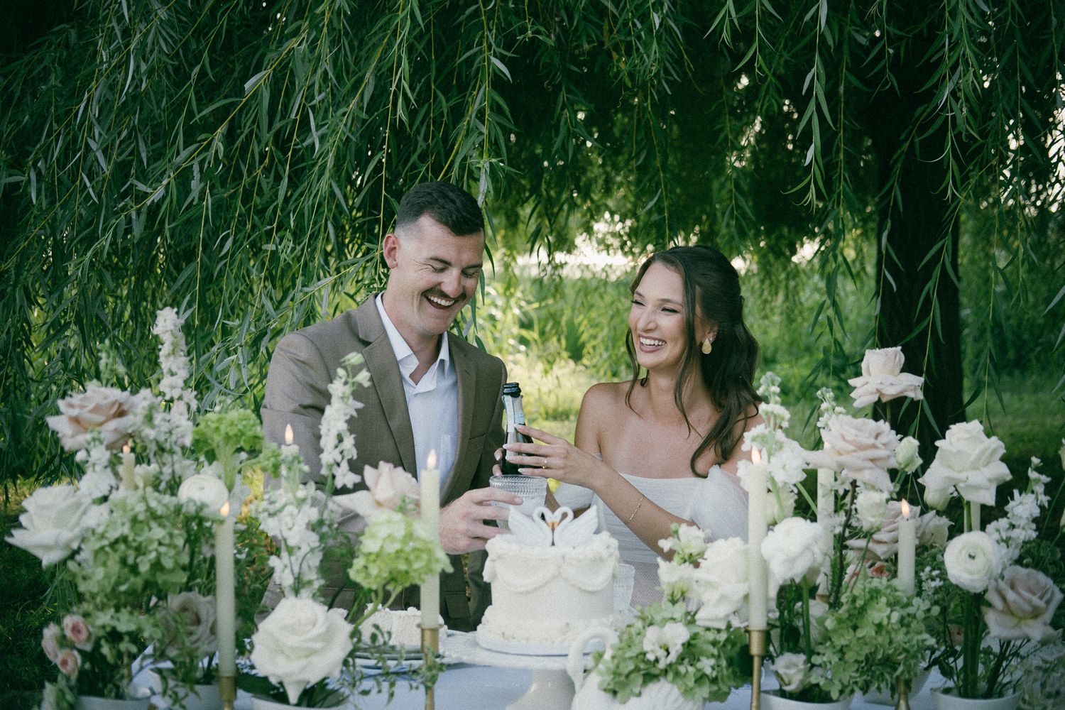 A bride and groom share romantic moments in a lush garden setting with elegant white floral arrangements and natural greenery.