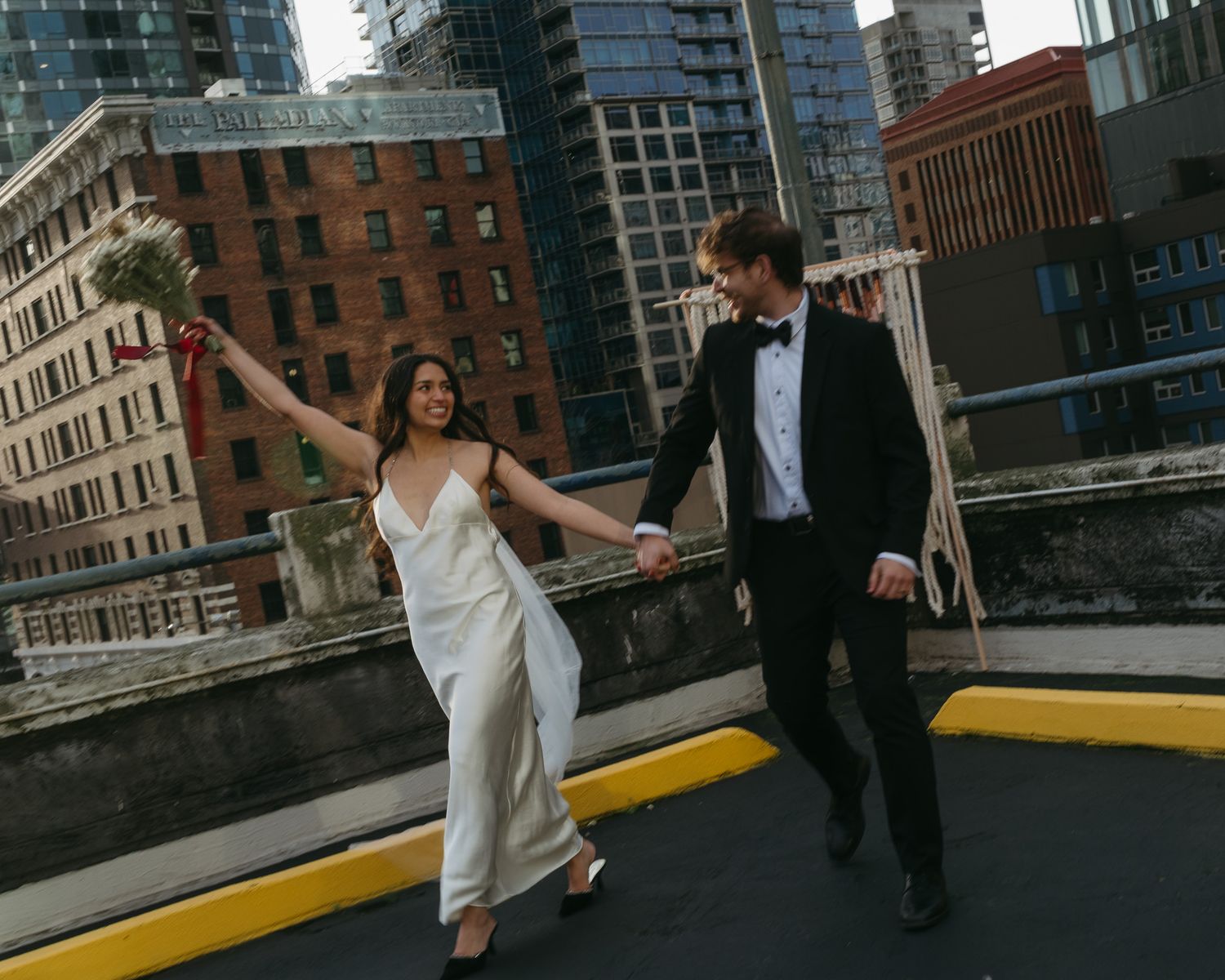 A newlywed couple dances celebrates their marriage on a rooftop in Seattle with urban buildings in the background.