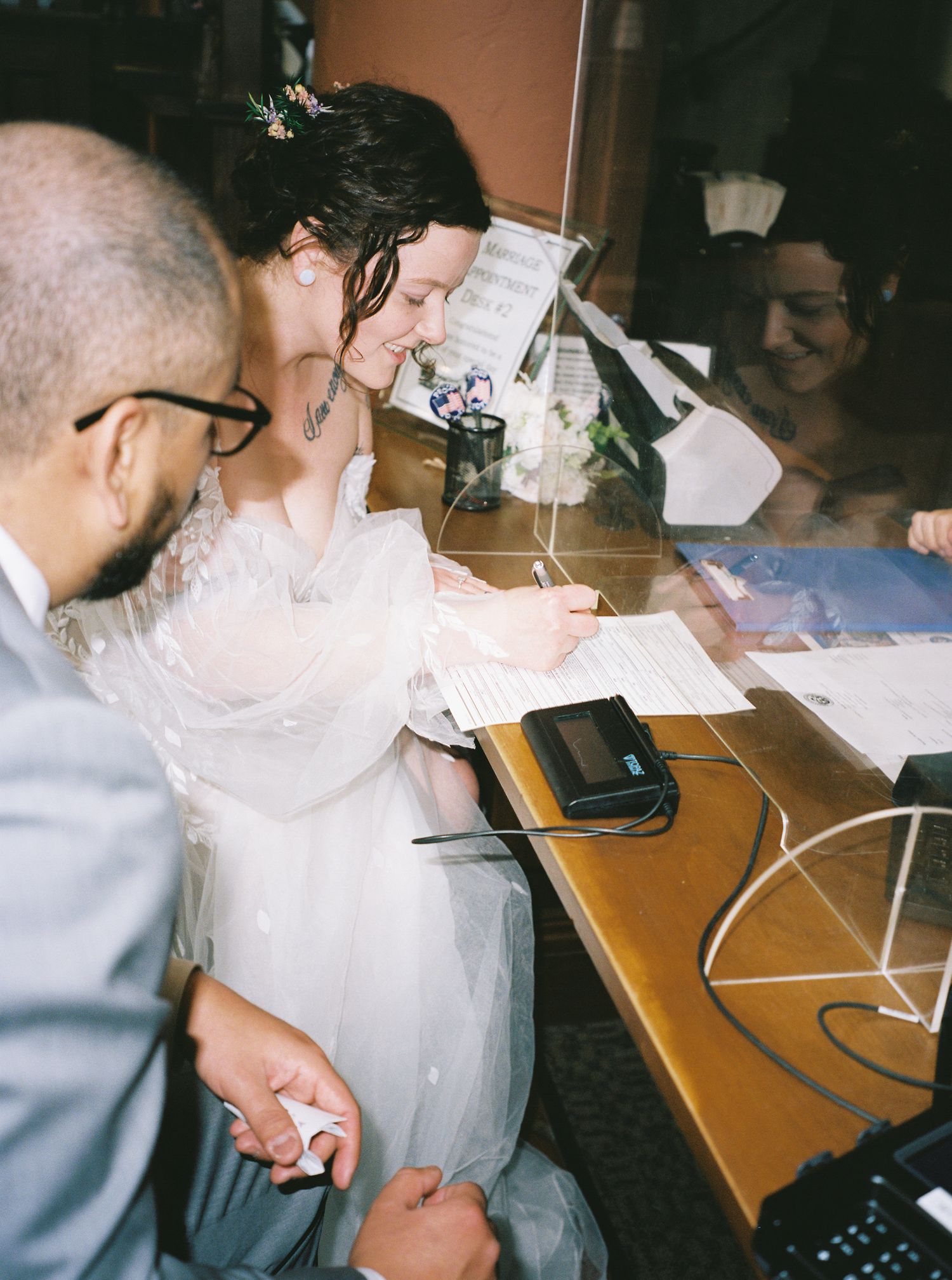 Two people work together at a desk with papers and electronics in a dimly lit office setting.