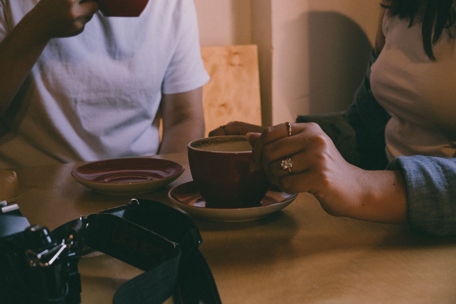 A detail shot of a womans engagement ring while her and her fiance drink coffee.