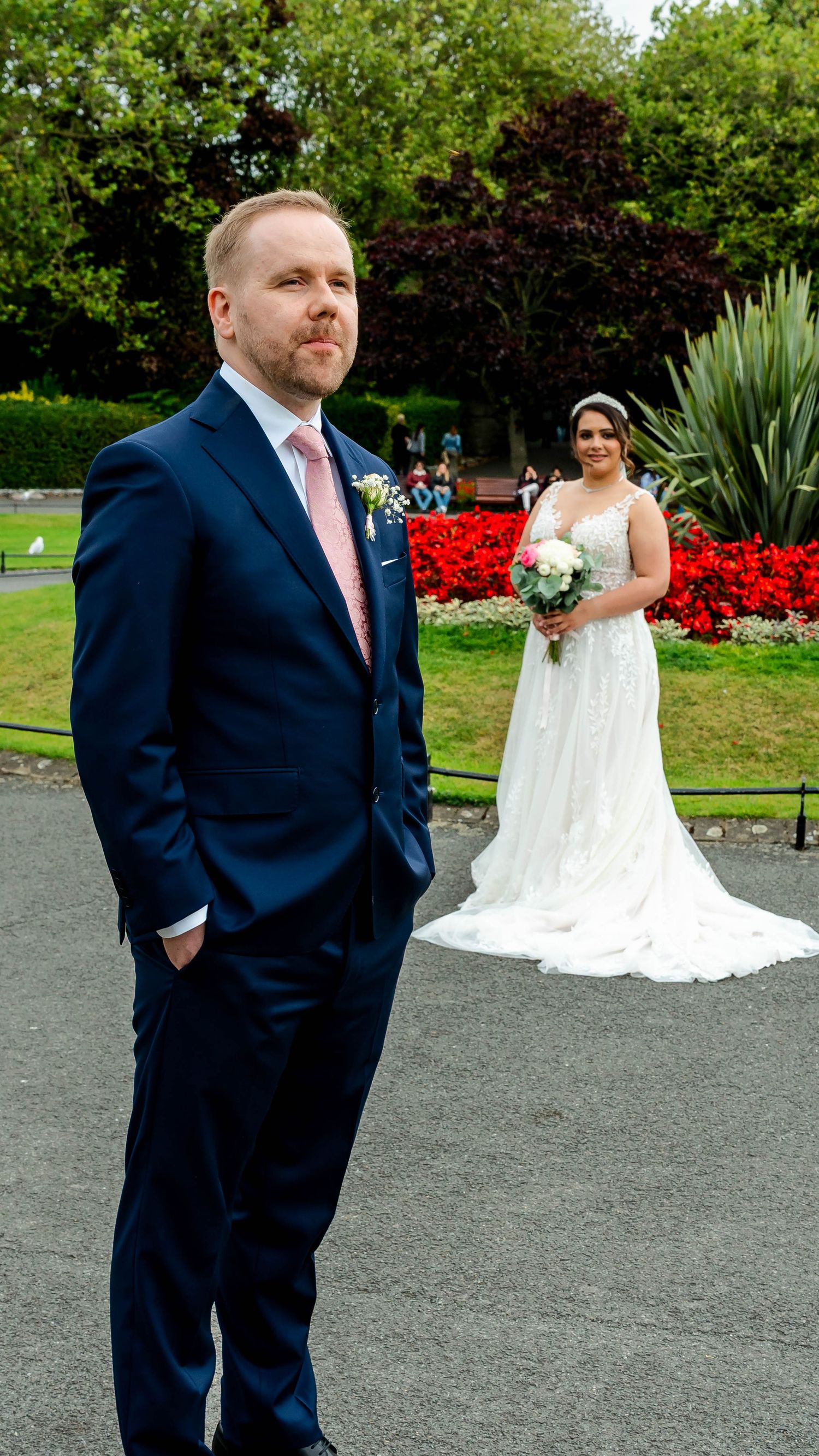 A couple poses for wedding photos in a garden with red flower beds and greenery.