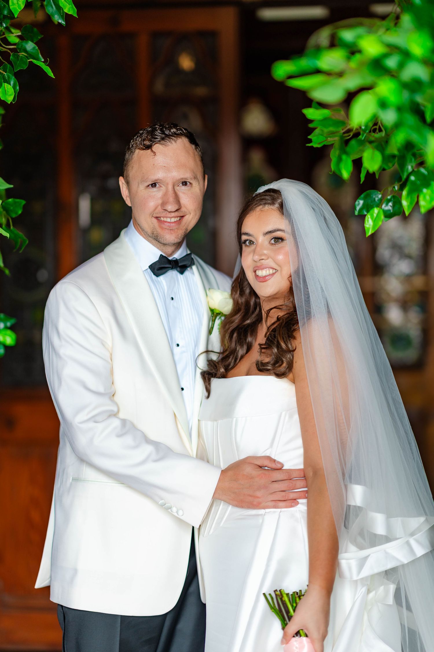 A bride and groom in white formal attire share a romantic moment together during their wedding celebration.