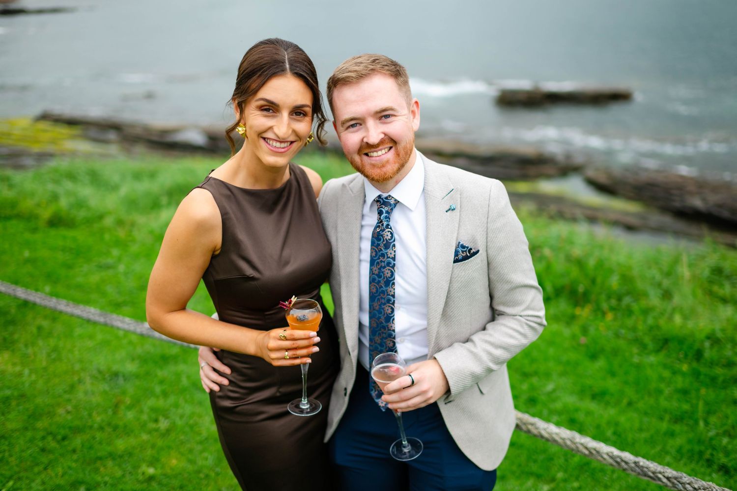 Guests in formal attire share laughs during outdoor celebration near waterfront.