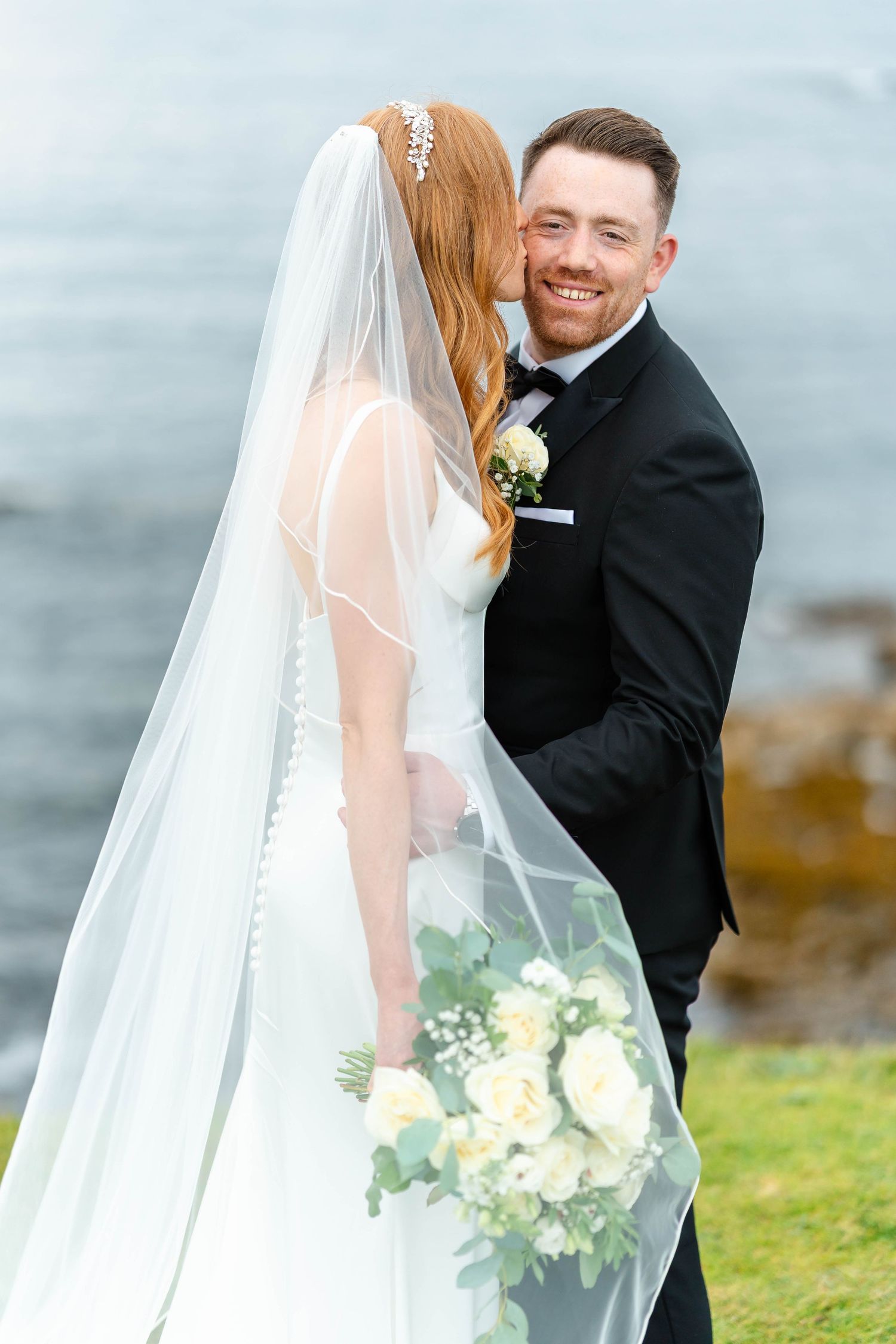 Romantic wedding moment captured against misty ocean background.