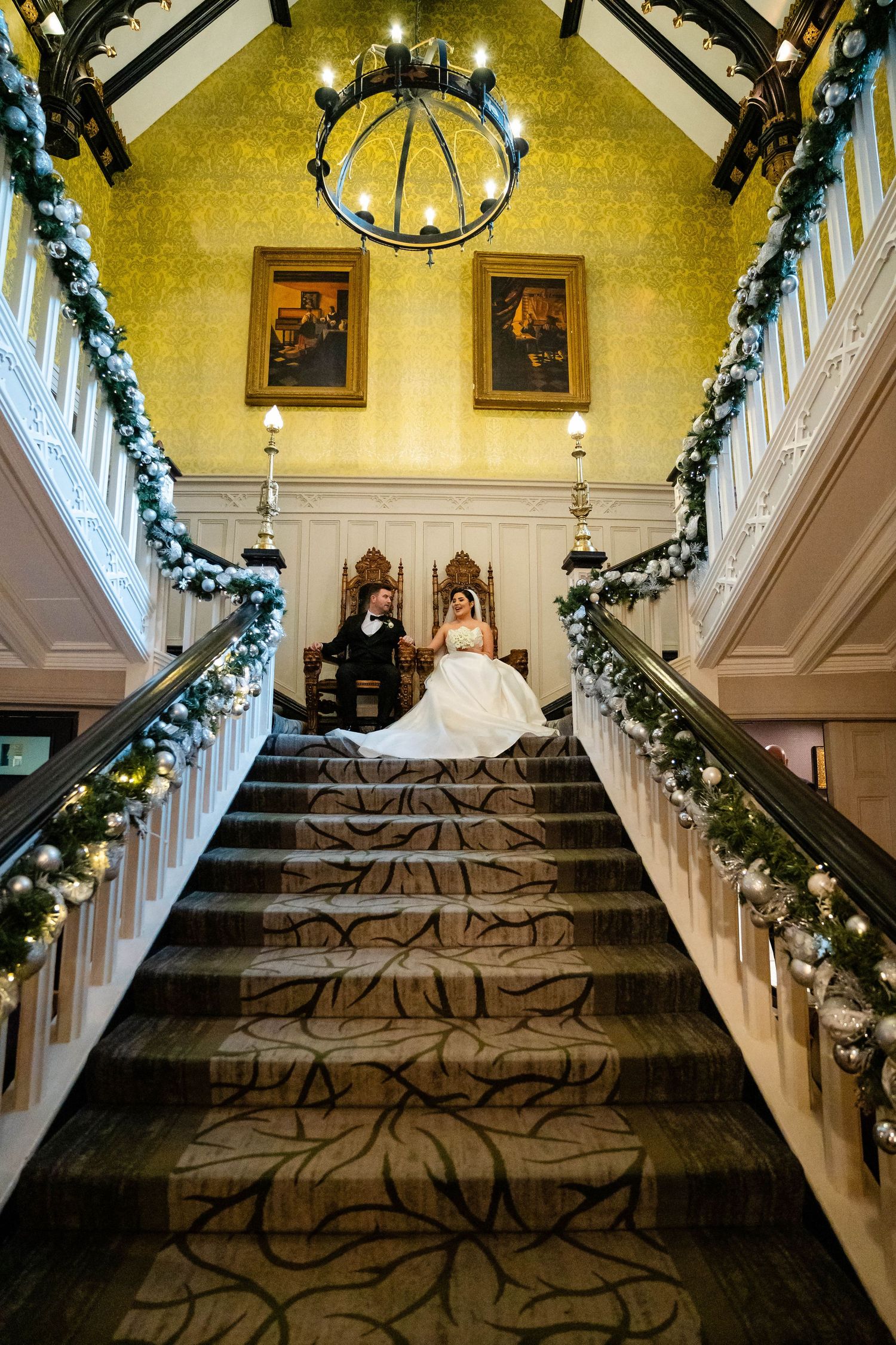 An elegant staircase decorated with Christmas garland and lights showcasing a beautiful wedding dress.