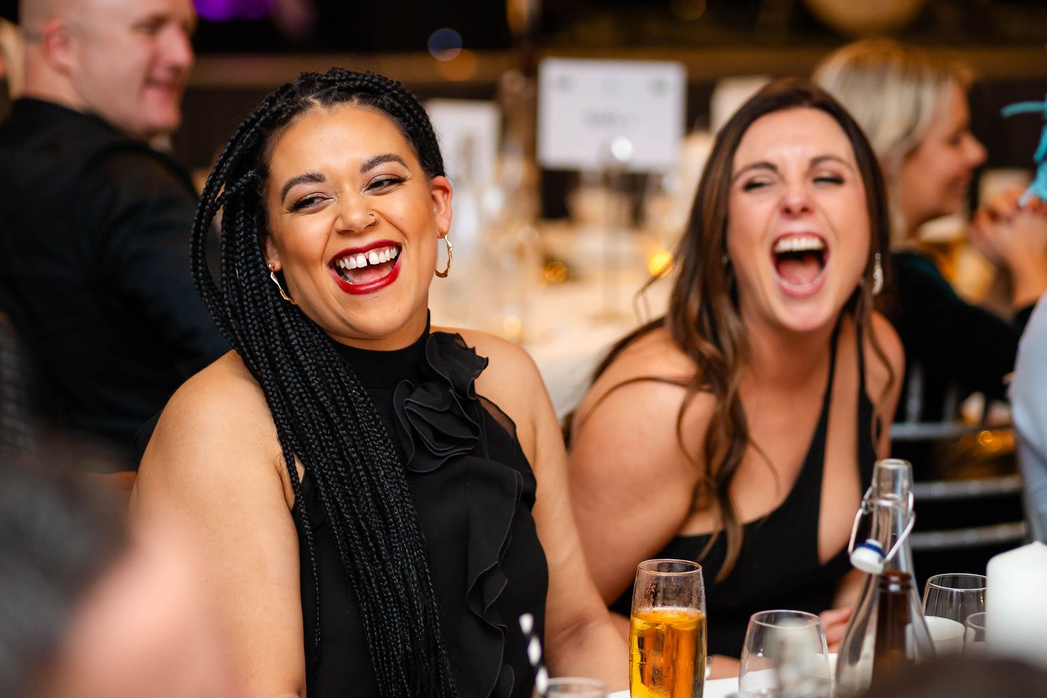 Wedding reception guests laughing and celebrating at dinner table.