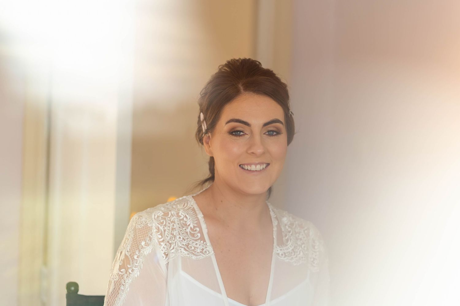 Person in white lace robe smiling during wedding preparations.