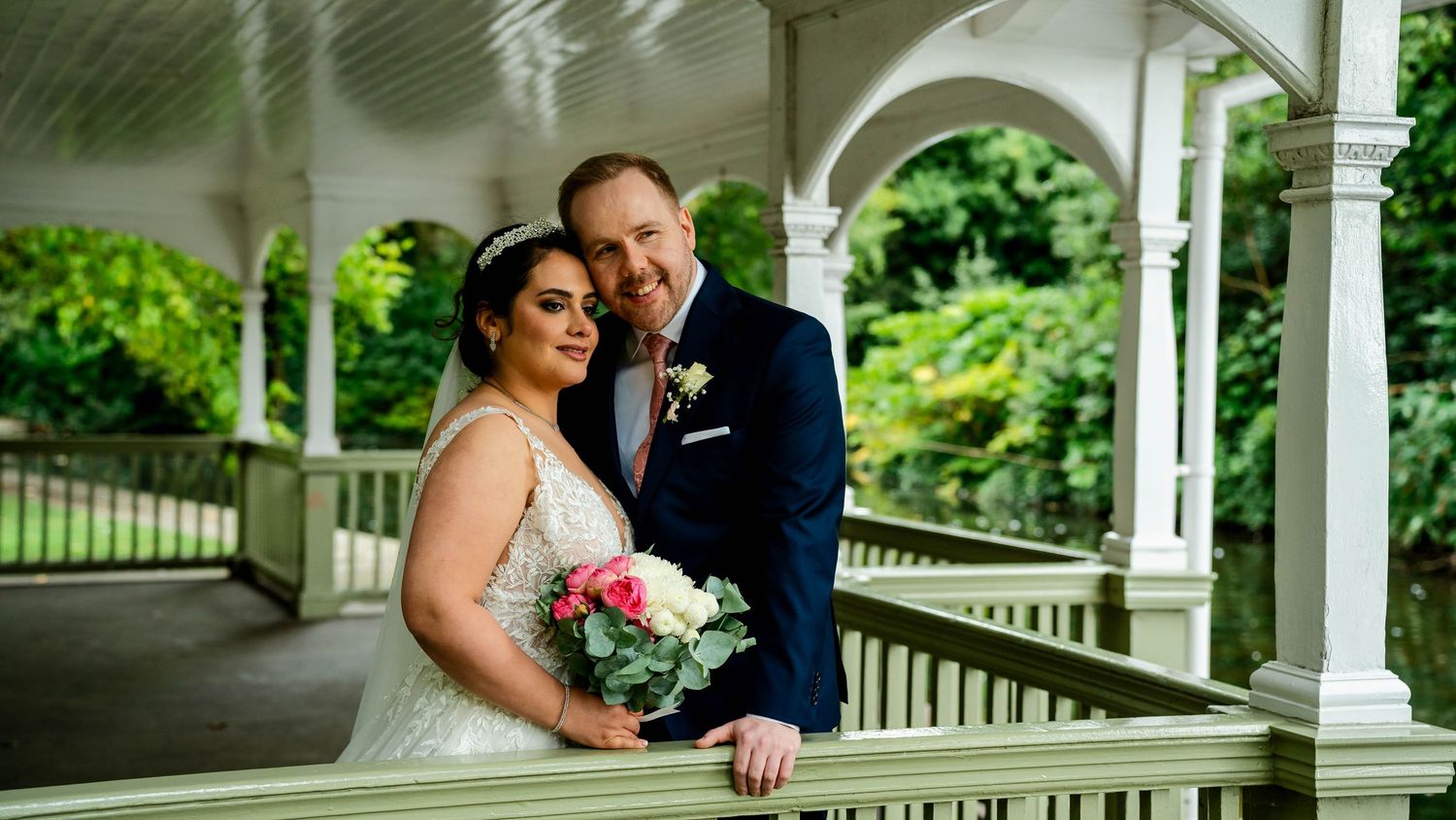 Wedding couple poses under an elegant white gazebo with classical columns.