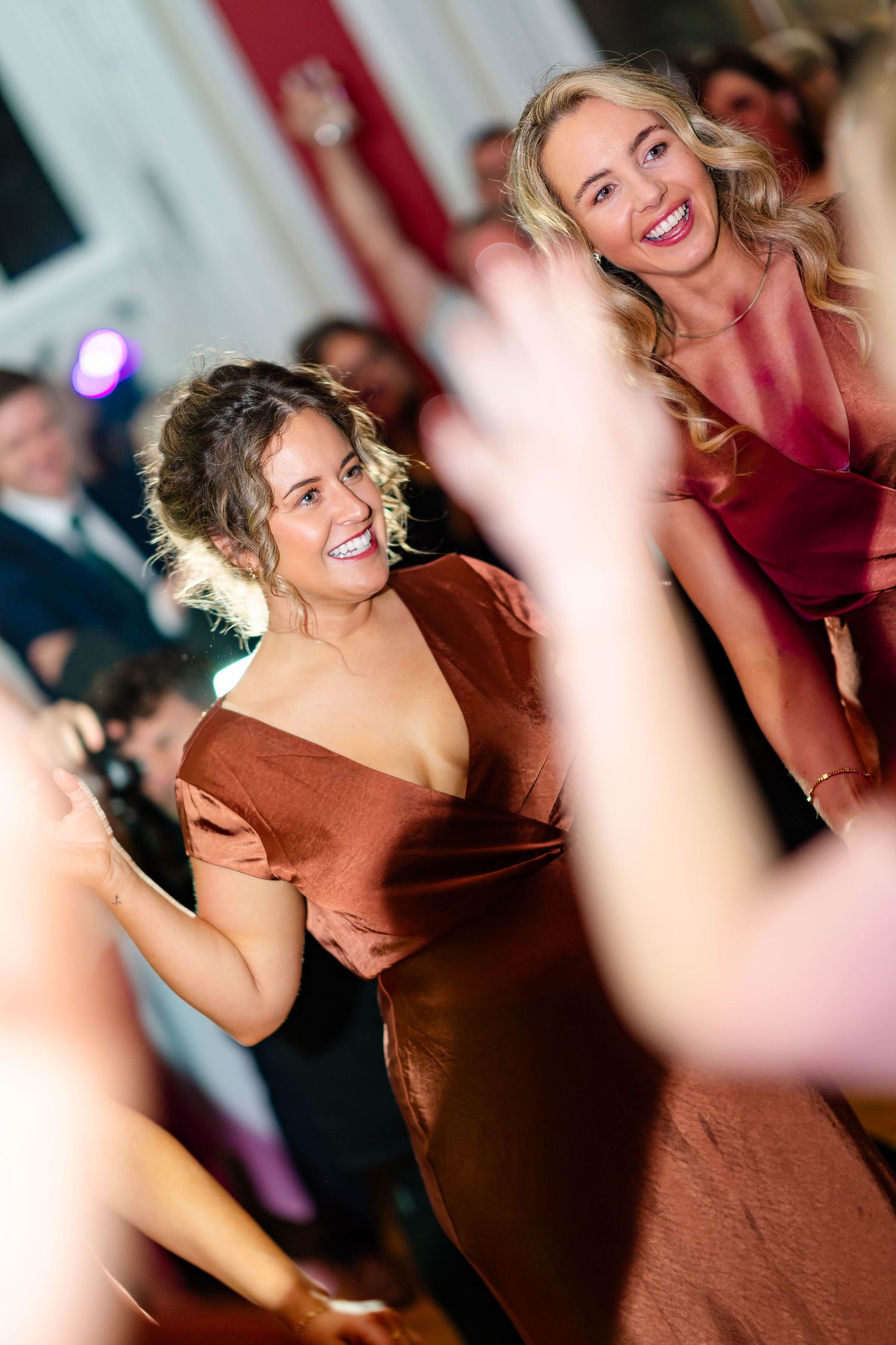 A person in a brown dress smiles and dances at a party with blurred background lighting and motion.