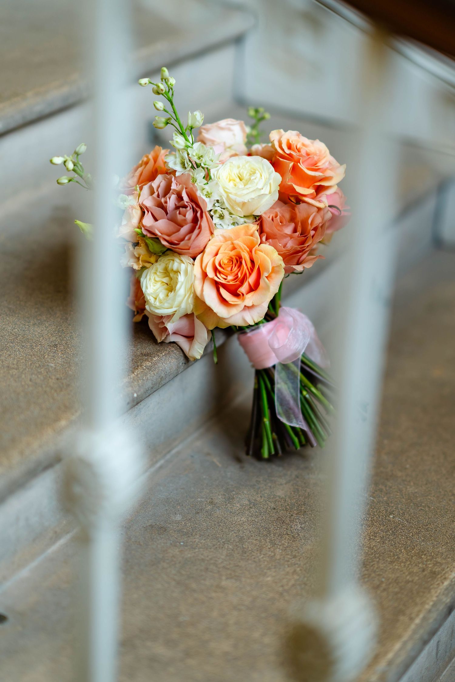 Small bouquet of peach and cream roses arranged with delicate greenery rests on a concrete surface.