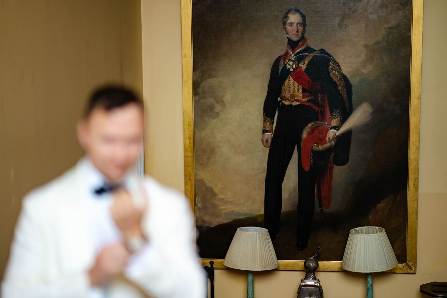 A row of formal portraits and paintings hang on a beige wall in an elegant gallery setting.
