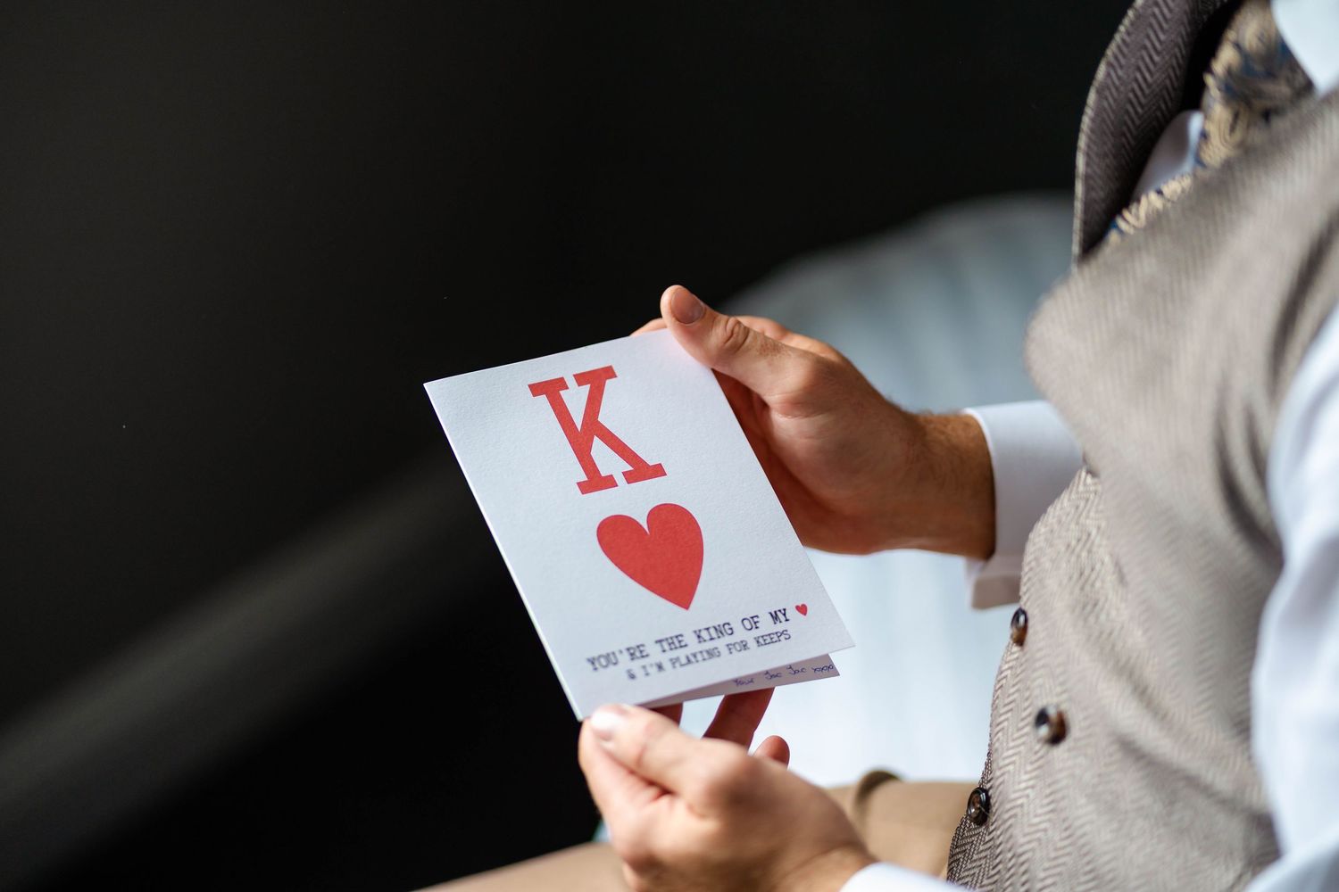 Hand holding a King of Hearts playing card against dark background.
