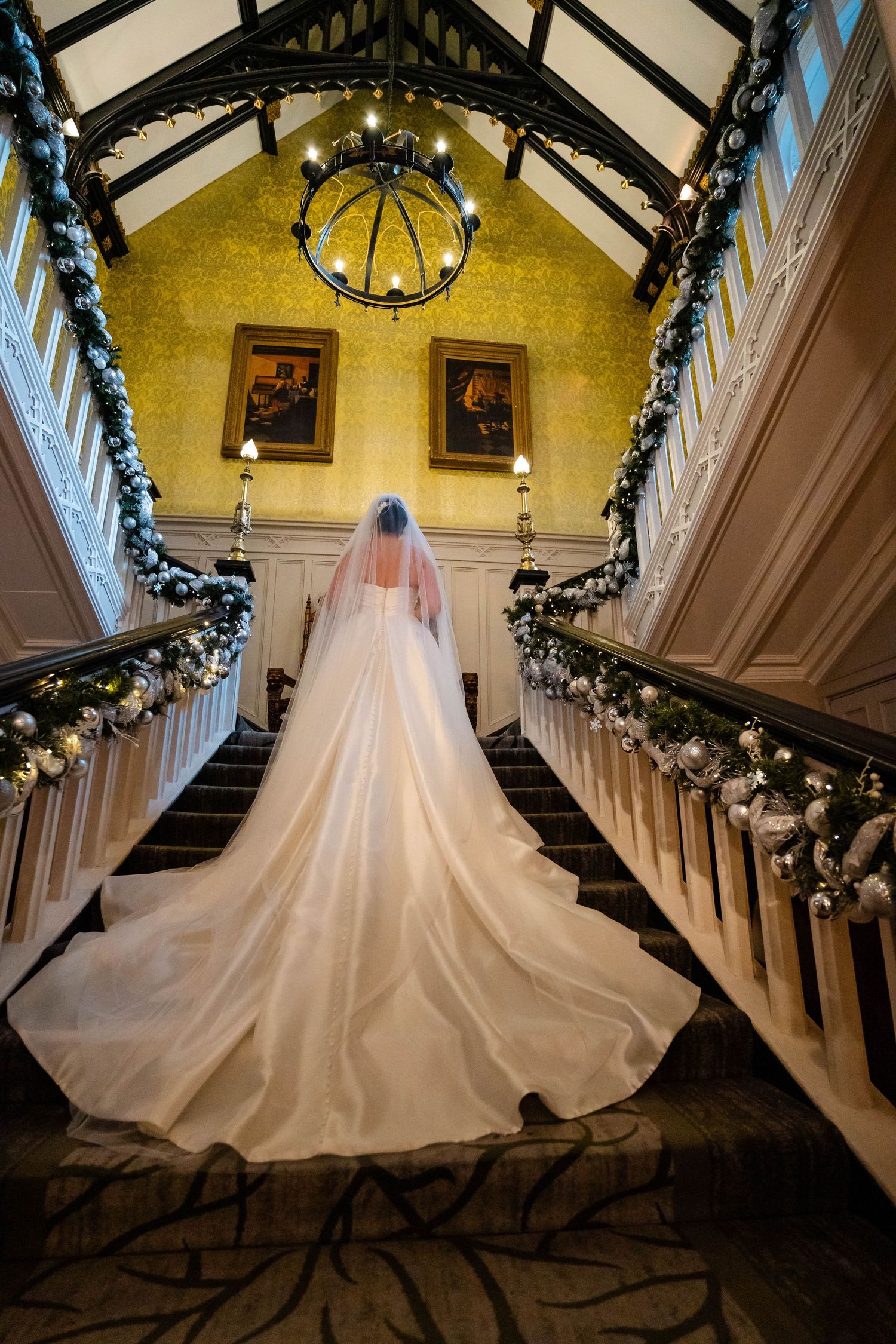 Dramatic view of bride's train on elegant staircase with yellow walls and holiday garland.