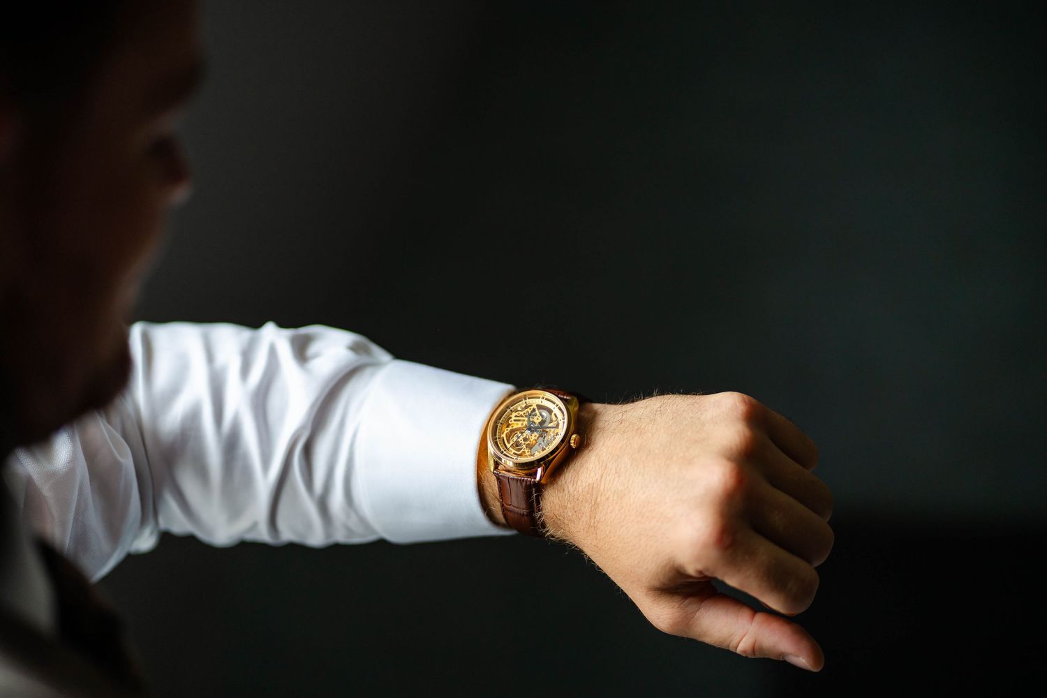 Close up of elegant gold watch on wrist with white shirt sleeve.